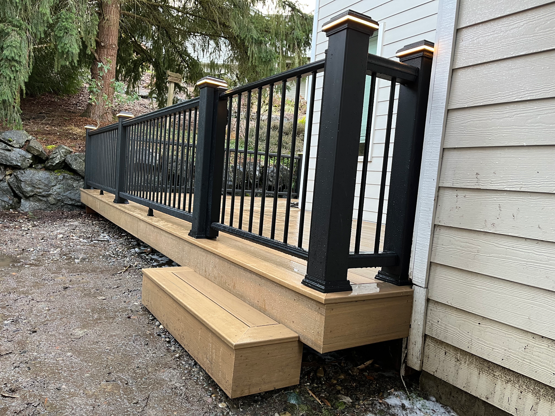 A wooden deck with a black railing and stairs next to a house.