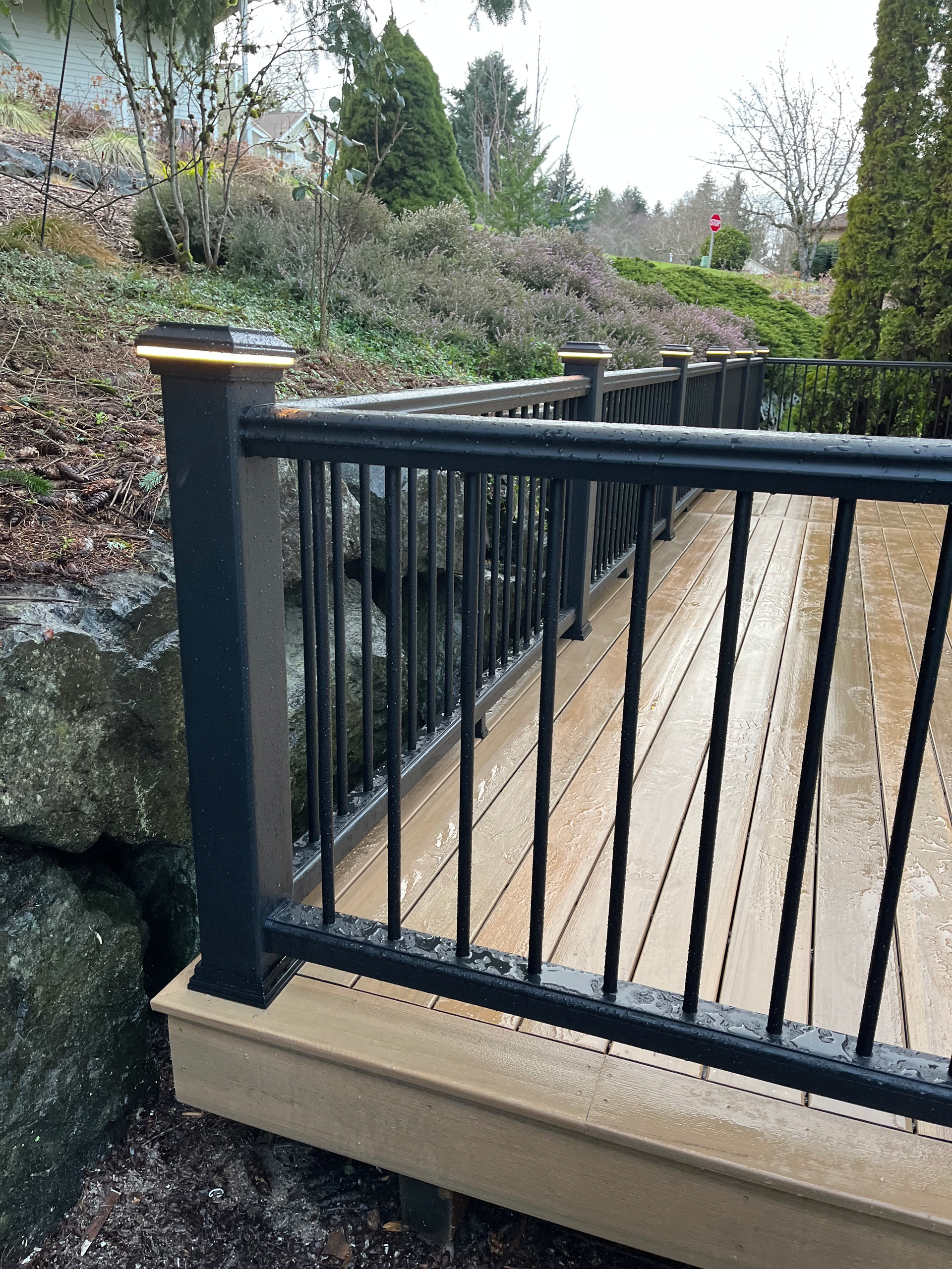 A wooden deck with a black railing is surrounded by rocks.