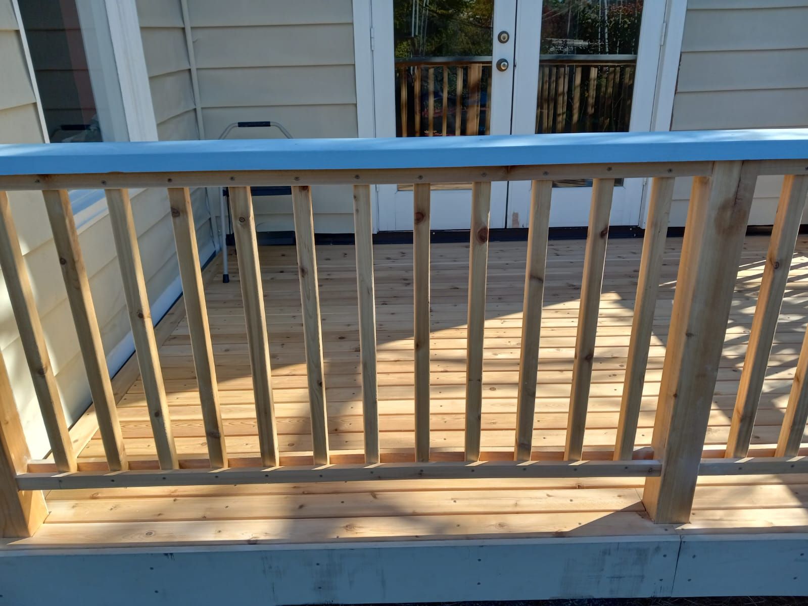 A wooden deck with a blue railing and a white house in the background.