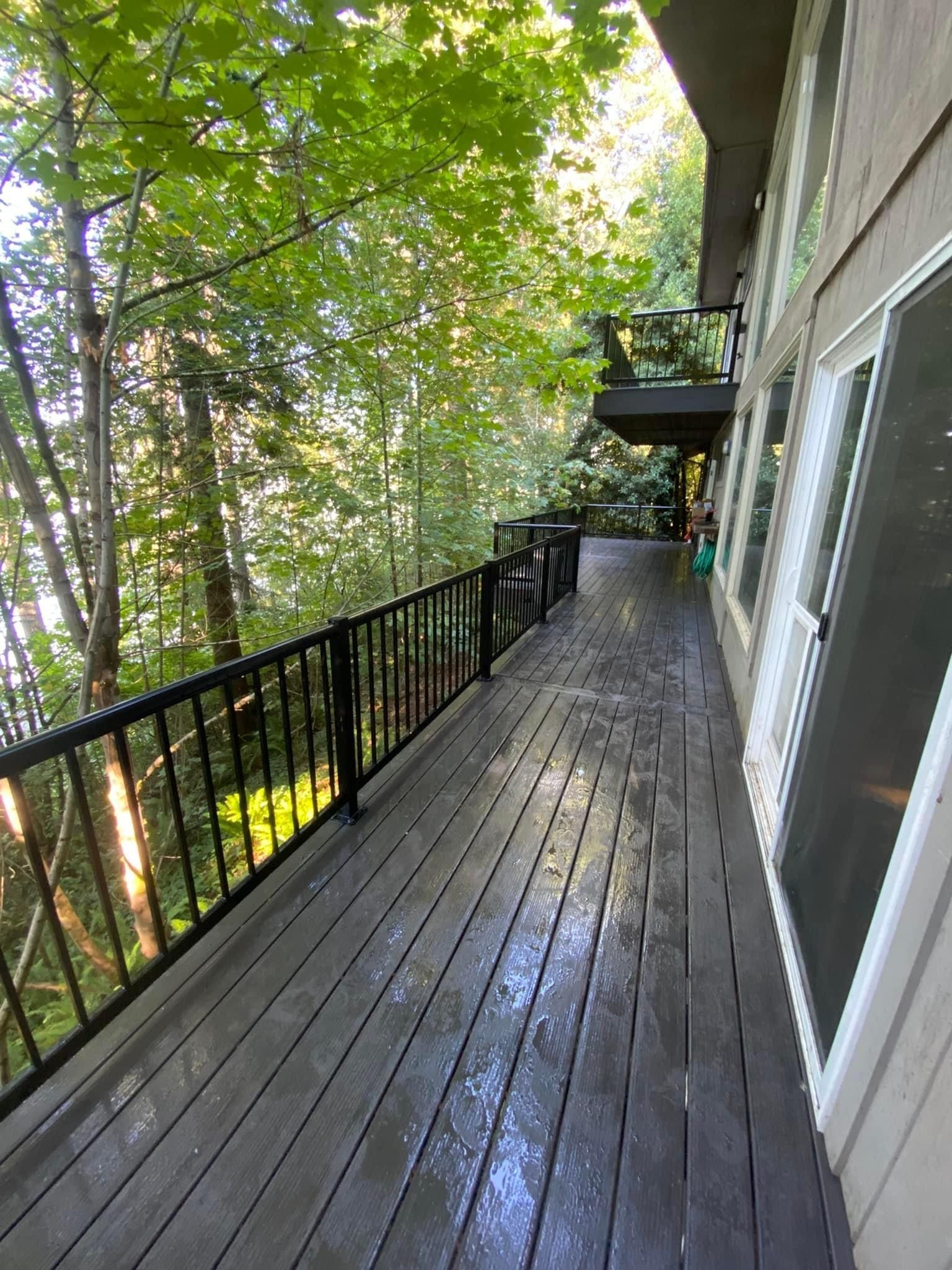 A large wooden deck with a black railing and trees in the background.