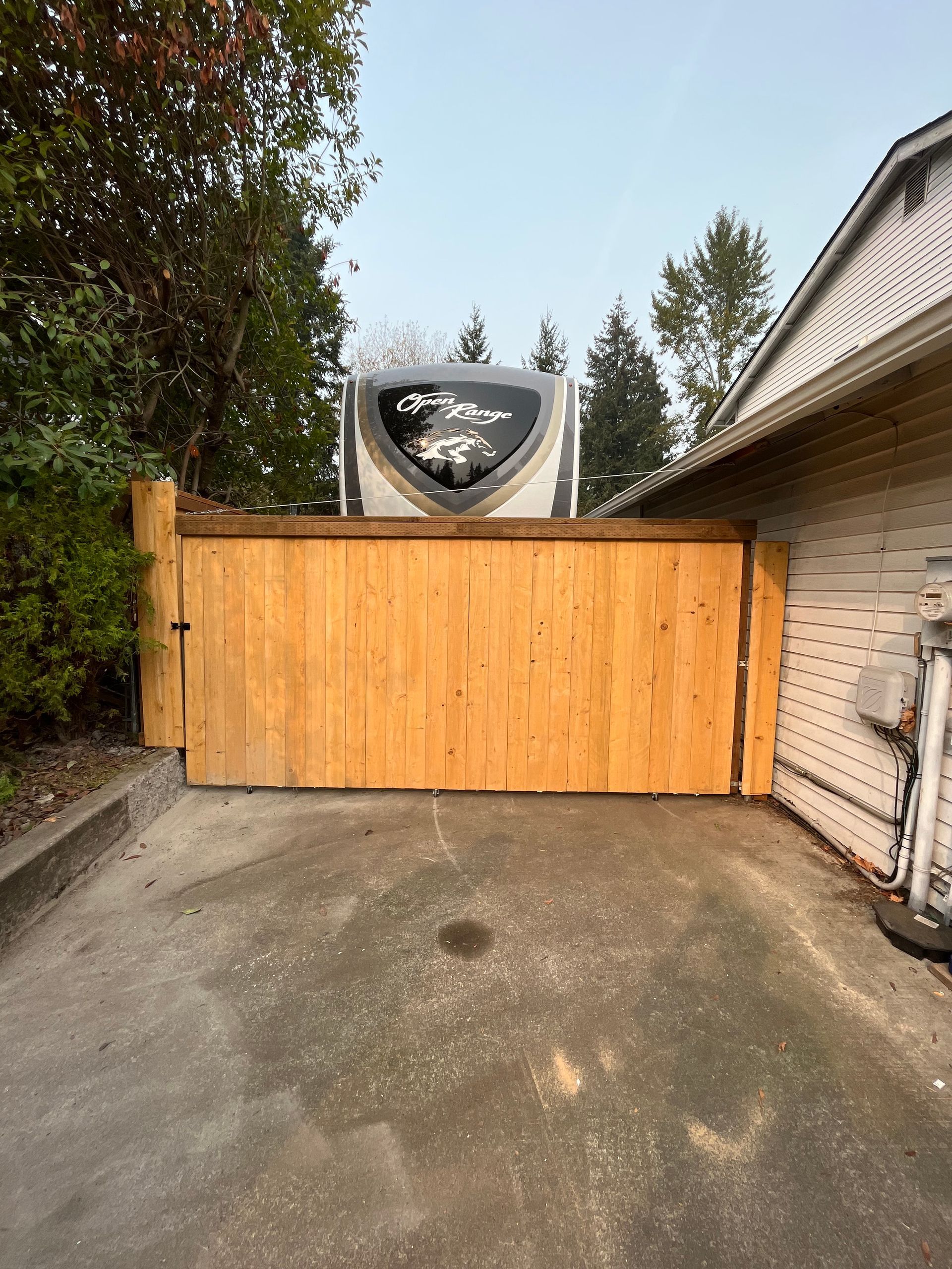 A trailer is parked behind a wooden gate in front of a house.