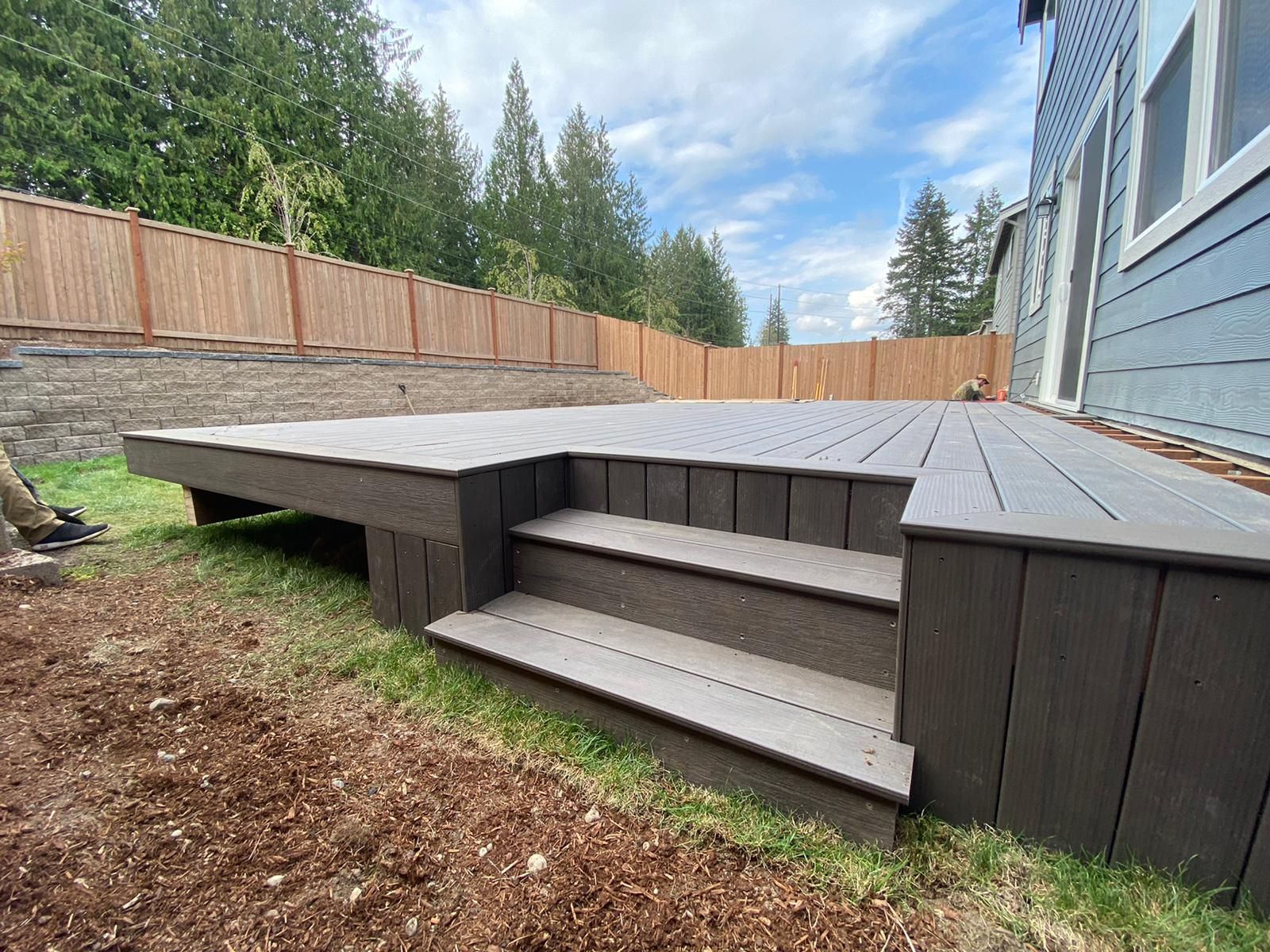 A deck with stairs leading up to it is in the backyard of a house.