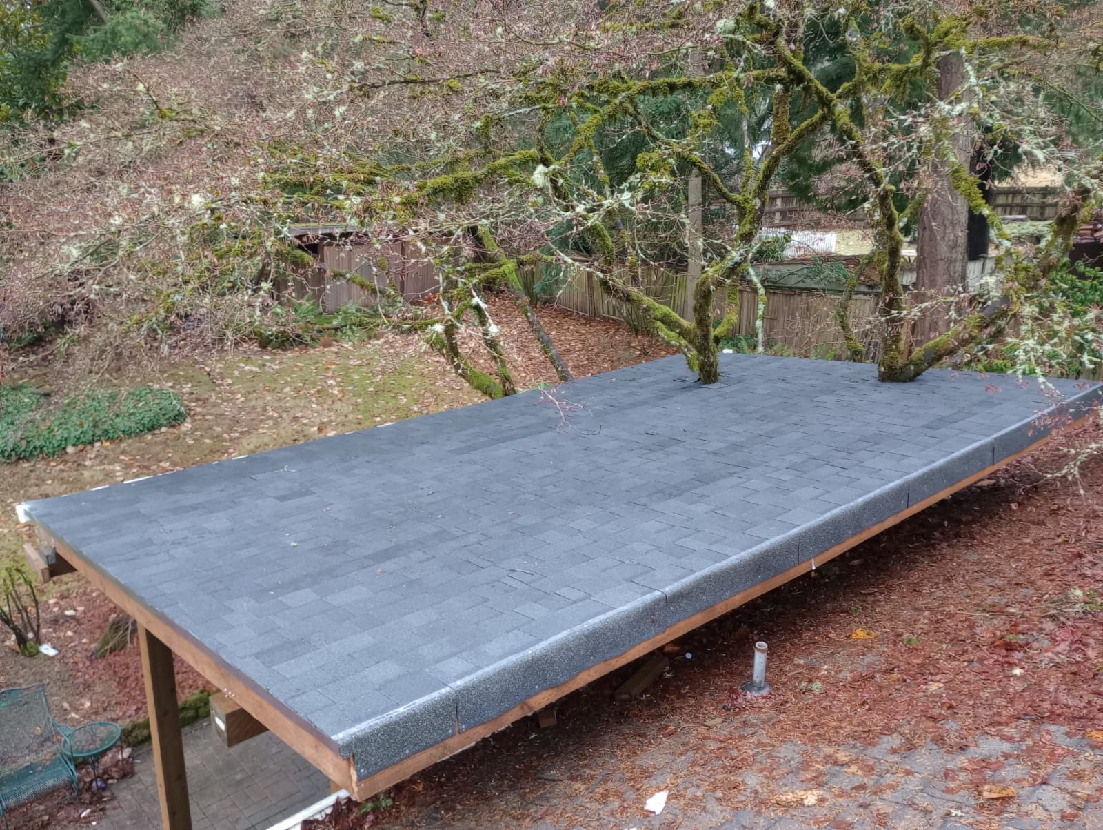 A wooden table with a gray roof is sitting in the woods.