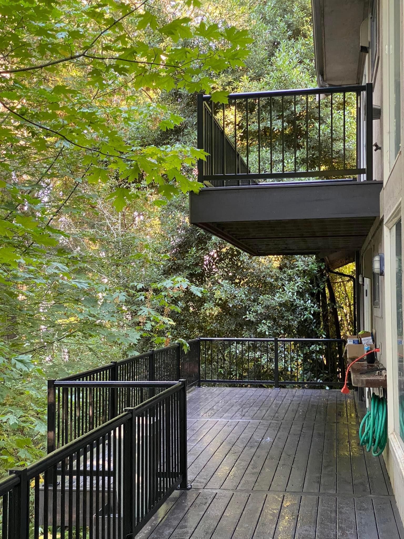 A large deck with a black railing is surrounded by trees.