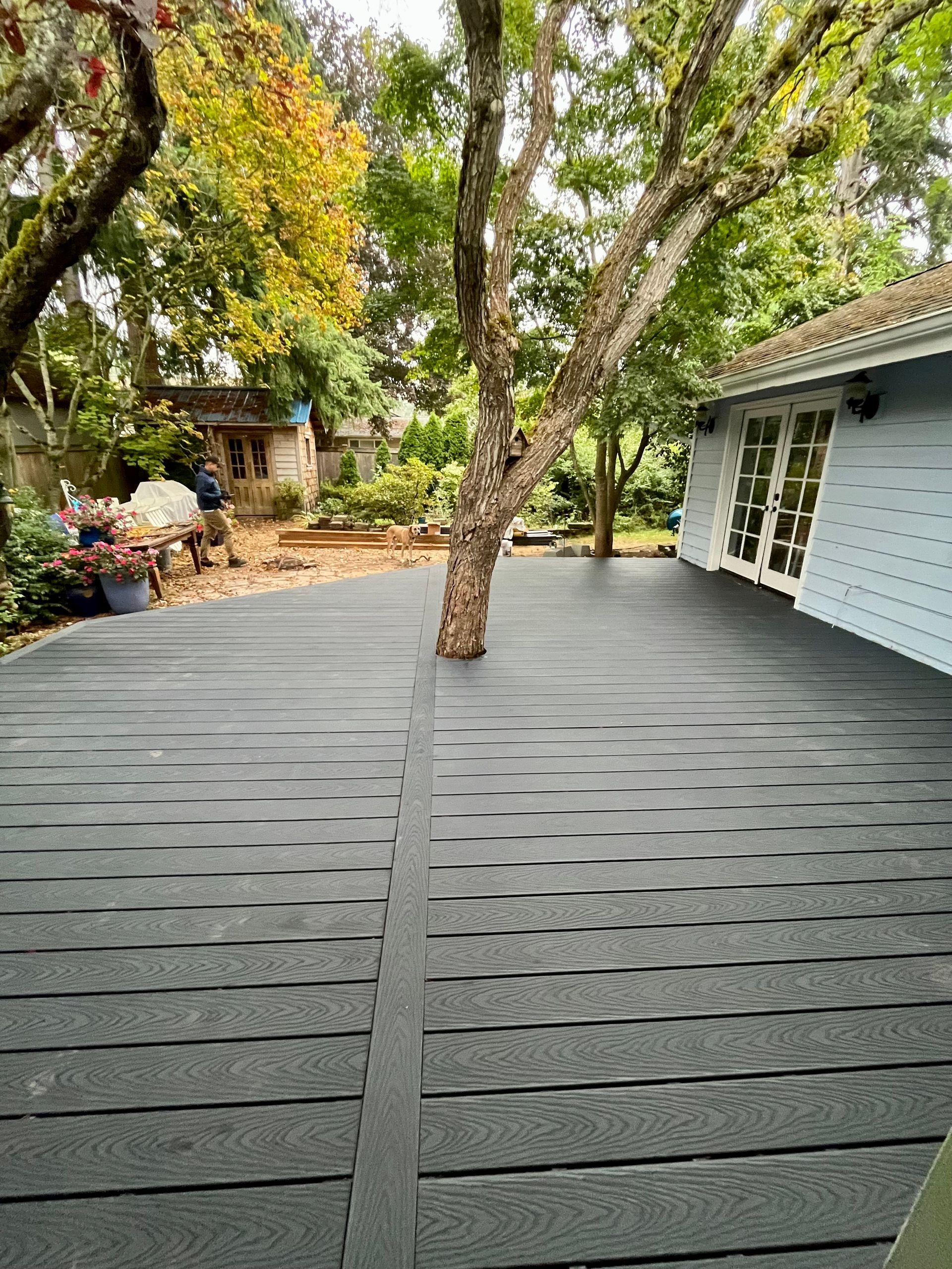 A black deck with a tree in the middle of it in front of a house.