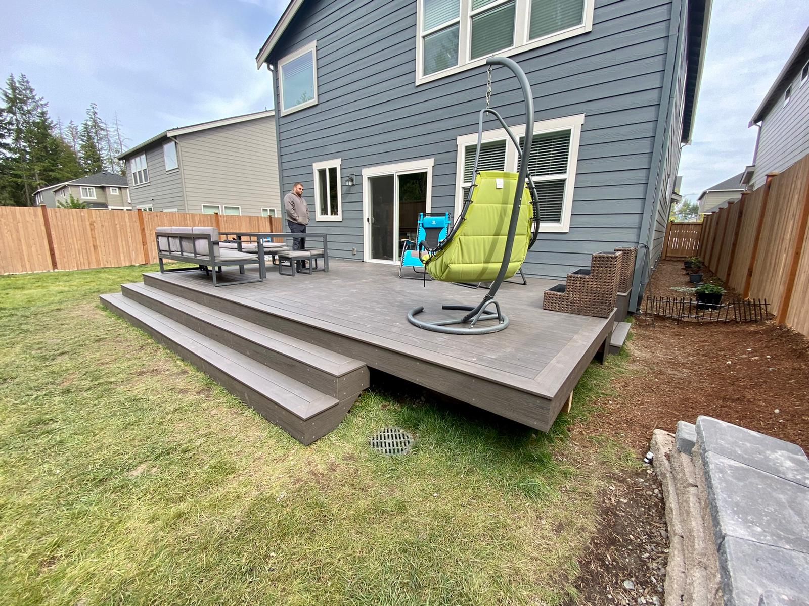 A man is standing on a deck in the backyard of a house.