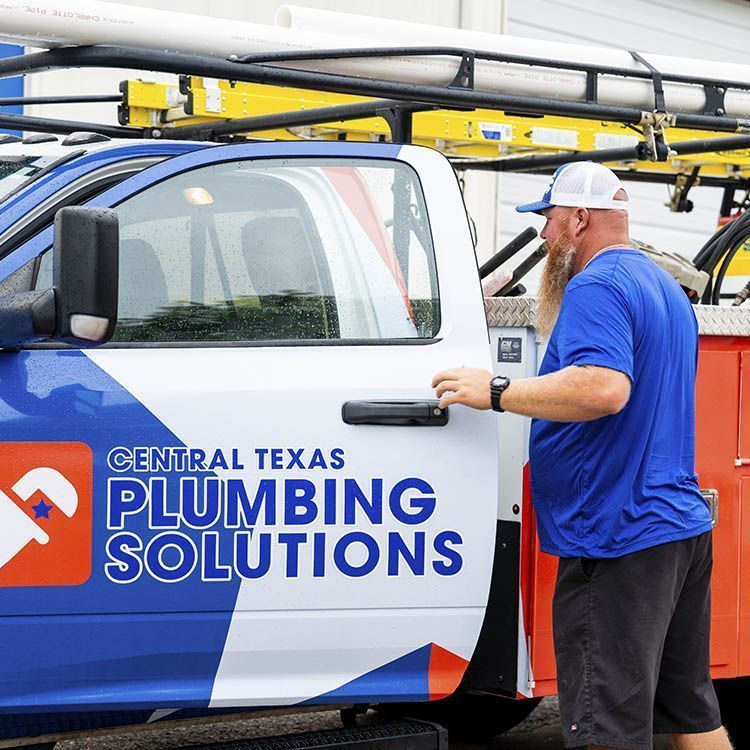 Man in blue shirt beside a Central Texas Plumbing Solutions truck, opening the door.