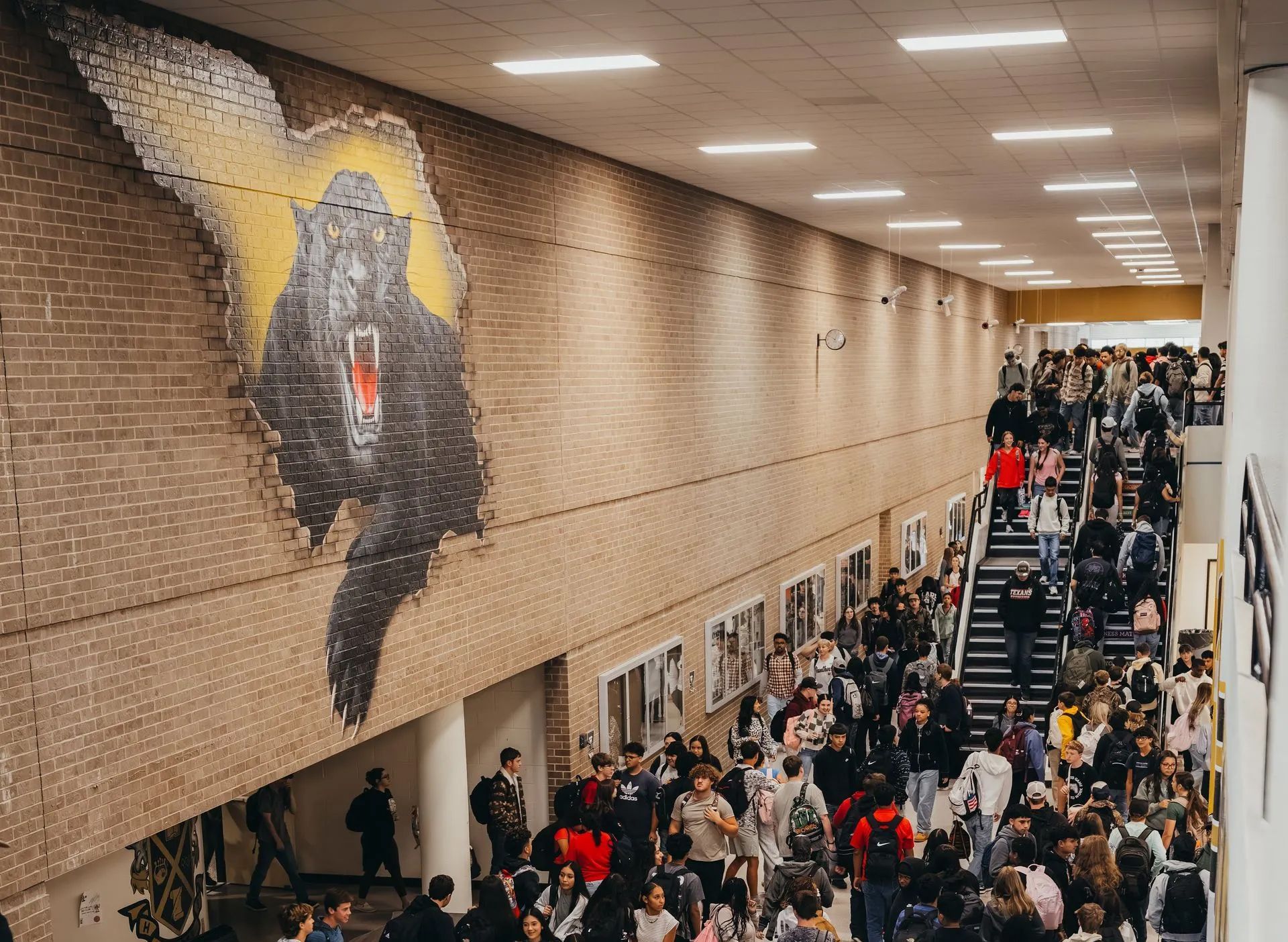 Large mural of a snarling bear on a brick wall in a school hallway filled with students.