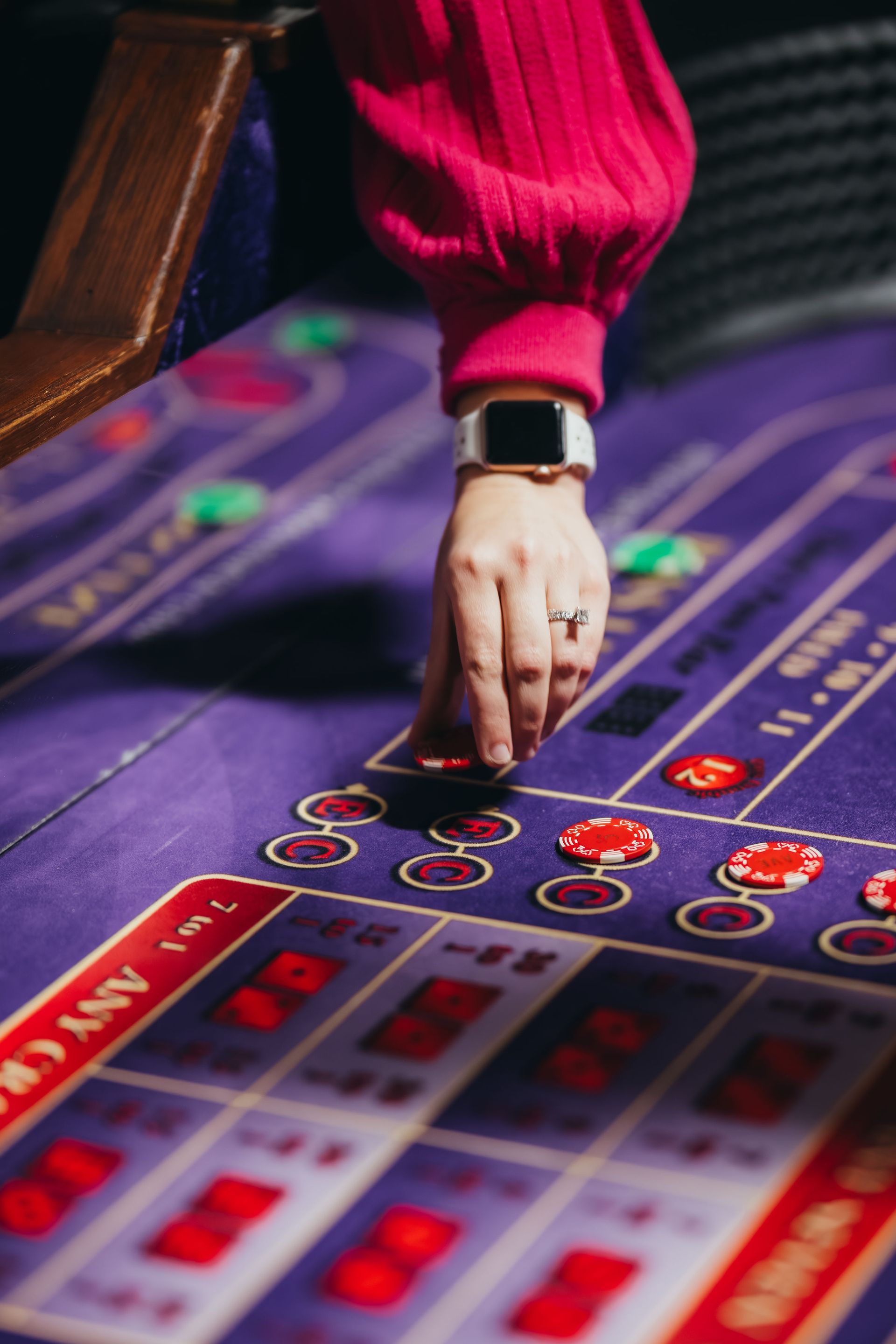 Person placing chips on a purple casino table. Hand with watch and ring. Red chips and table markings.