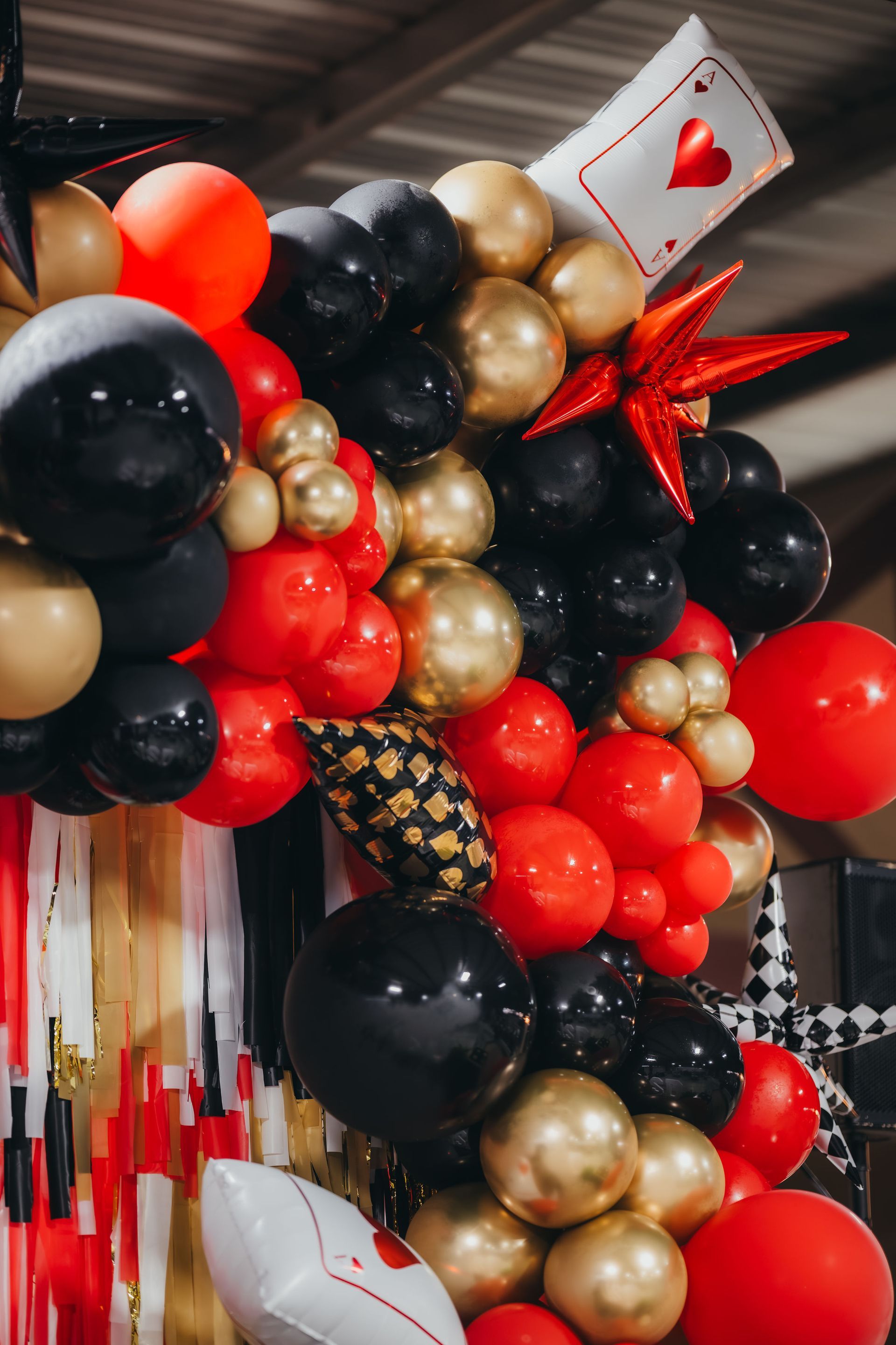 Balloon arch with red, black, and gold balloons, playing card accent.