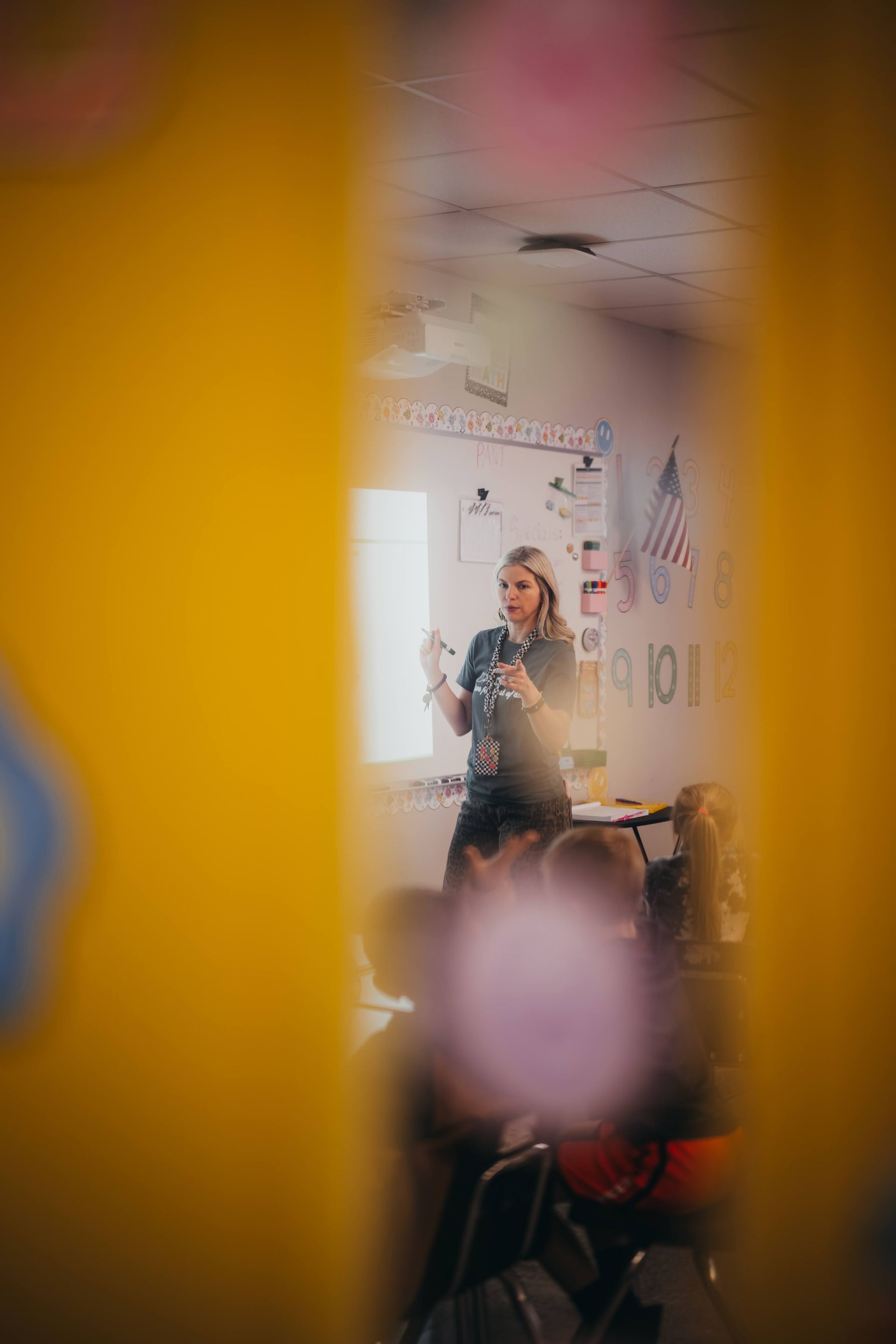 Teacher in a classroom, standing in front of students and a whiteboard. Classroom setting.