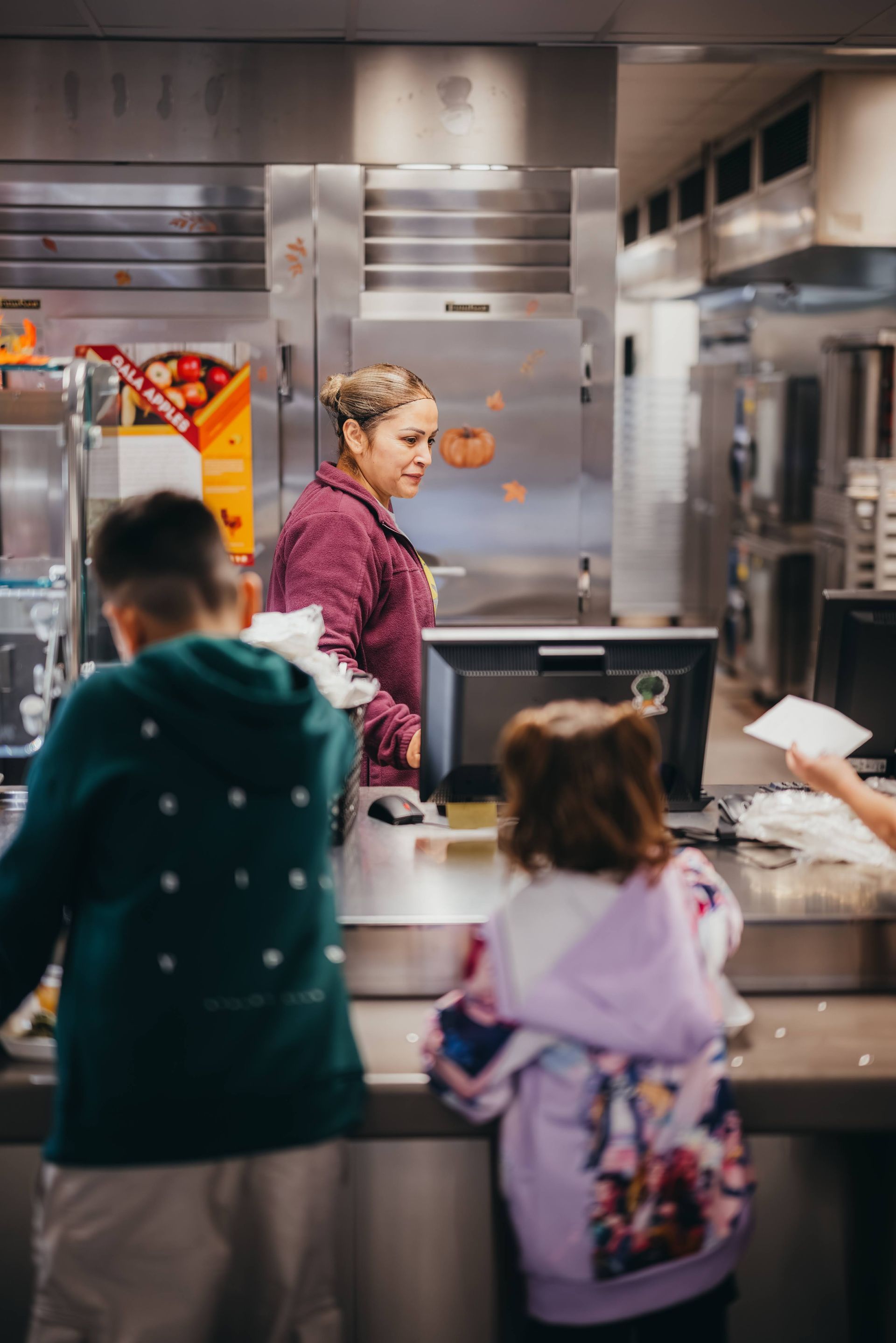 Woman serving children at a school cafeteria counter. Children stand in line.
