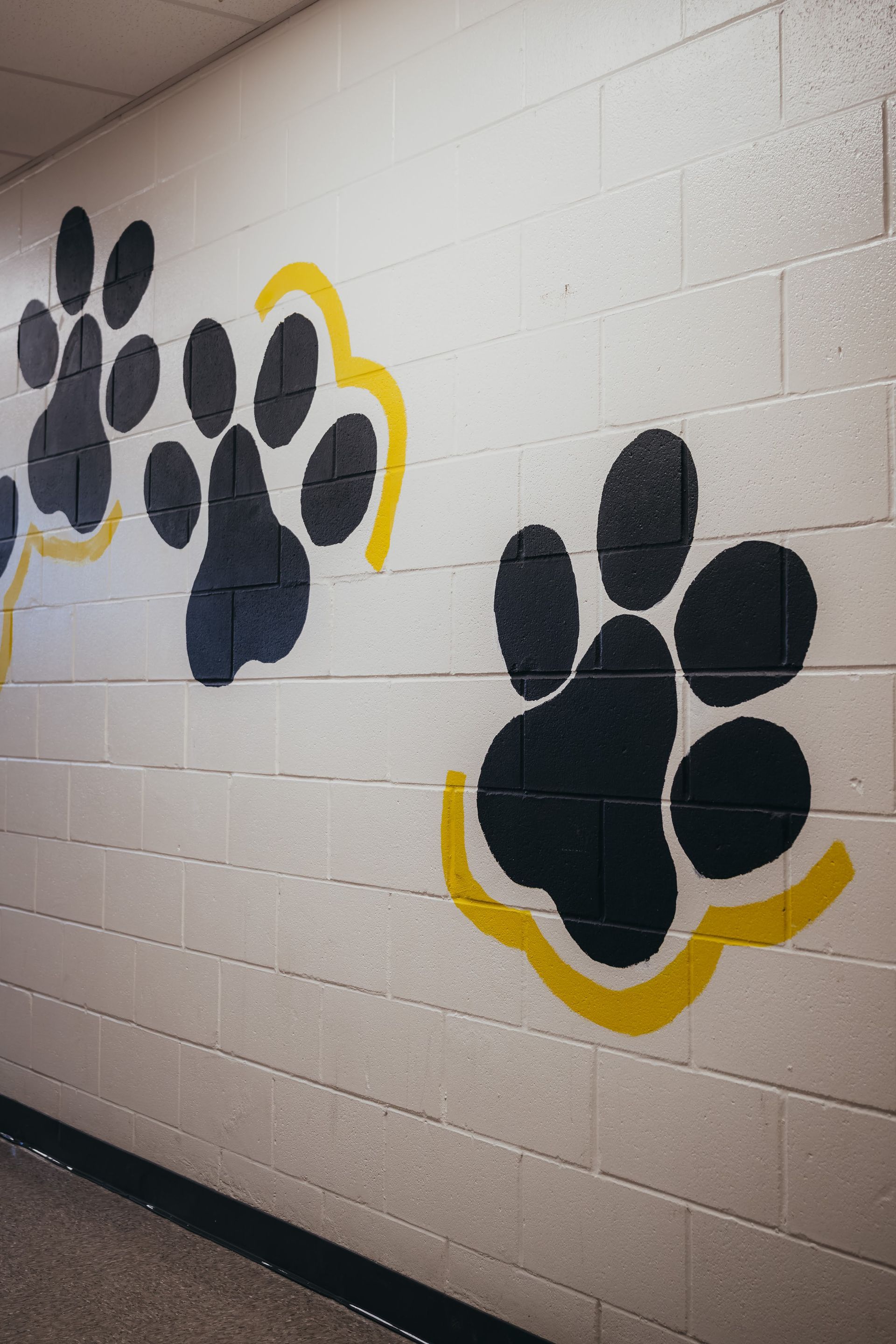 Black and yellow paw prints painted on a white brick wall in a hallway.