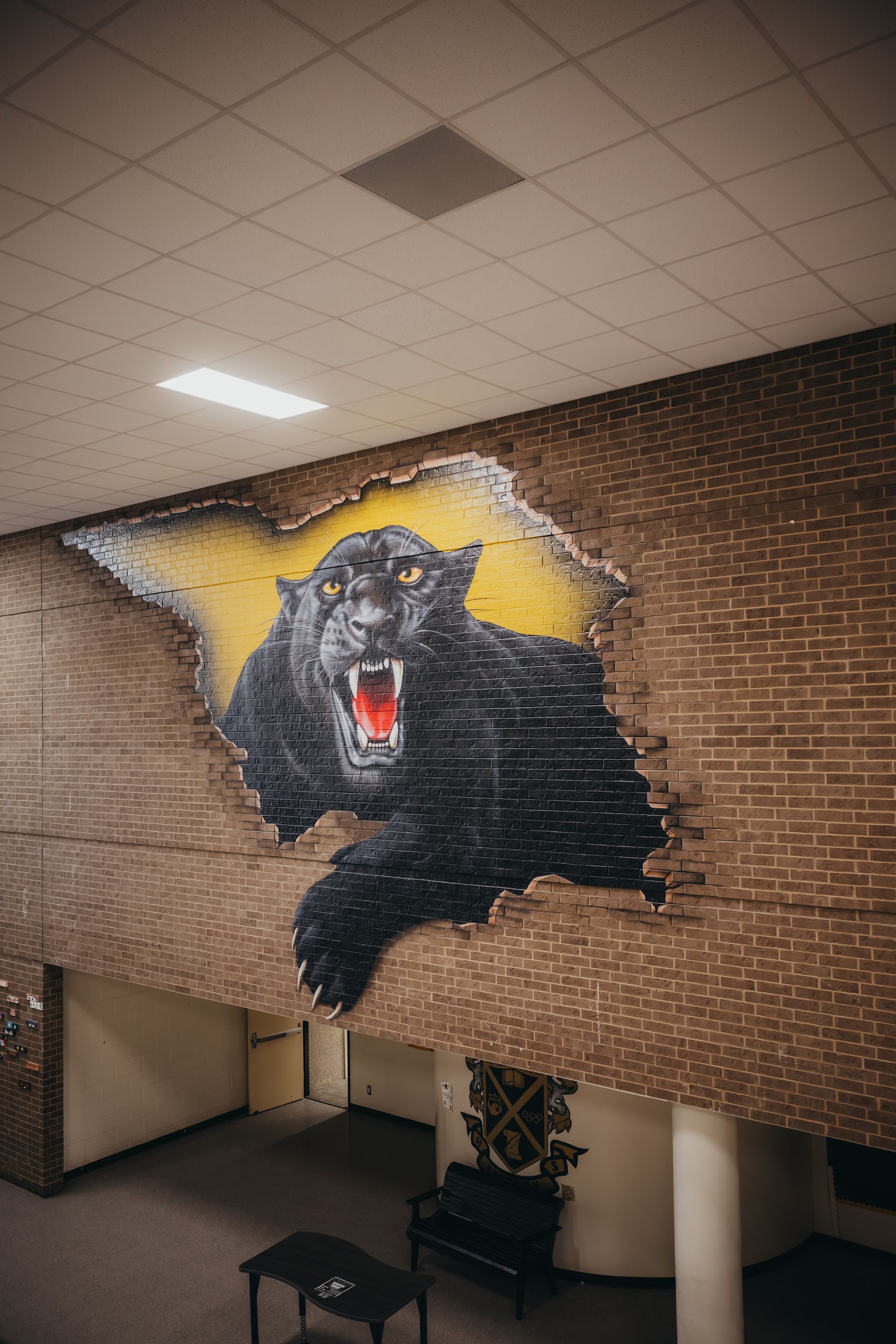 Black panther mural bursting through a brick wall, yellow backdrop, interior hallway.