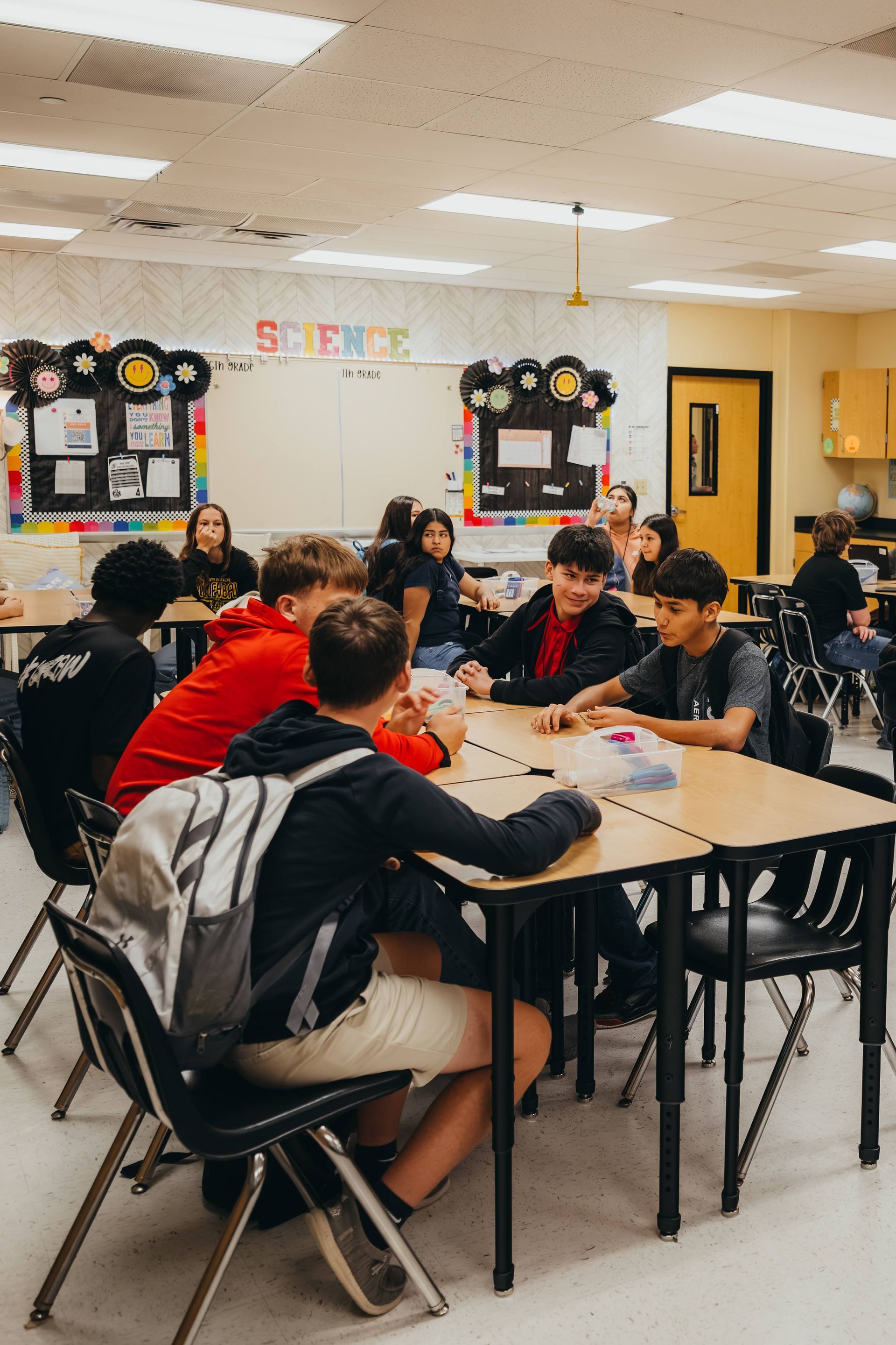 Students sitting around a desk in a classroom, talking.