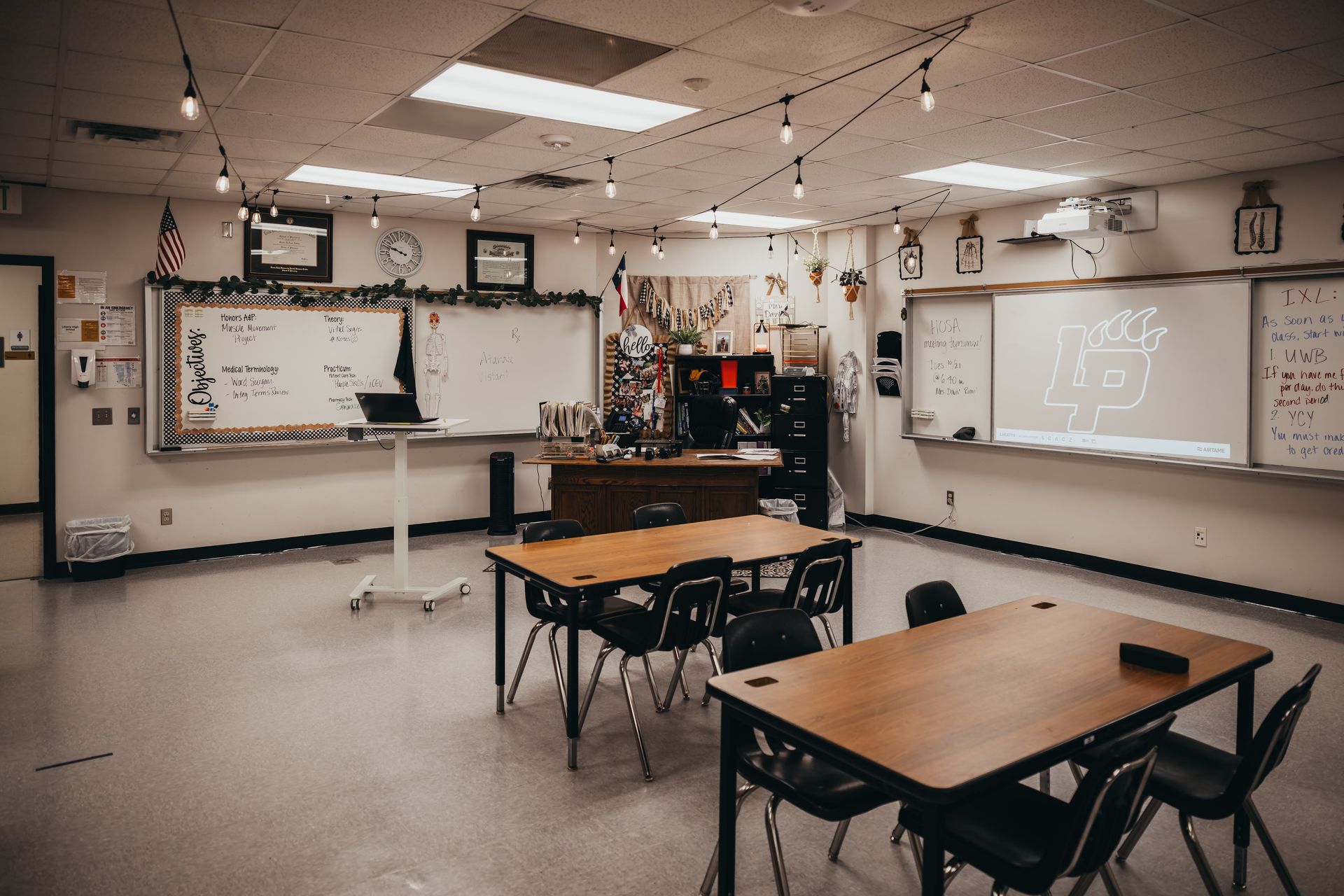 Empty classroom with two student desks, whiteboards, and string lights.