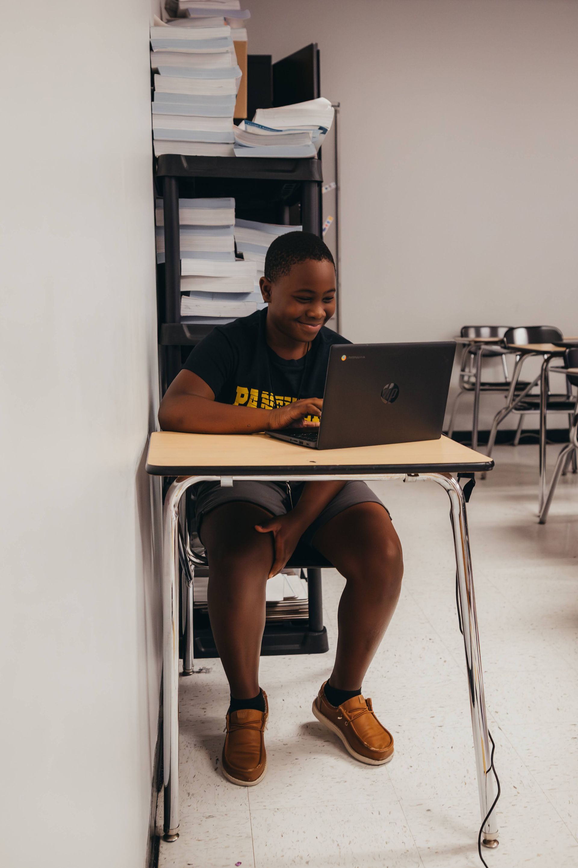 Student using a laptop at a desk in a classroom, smiling.