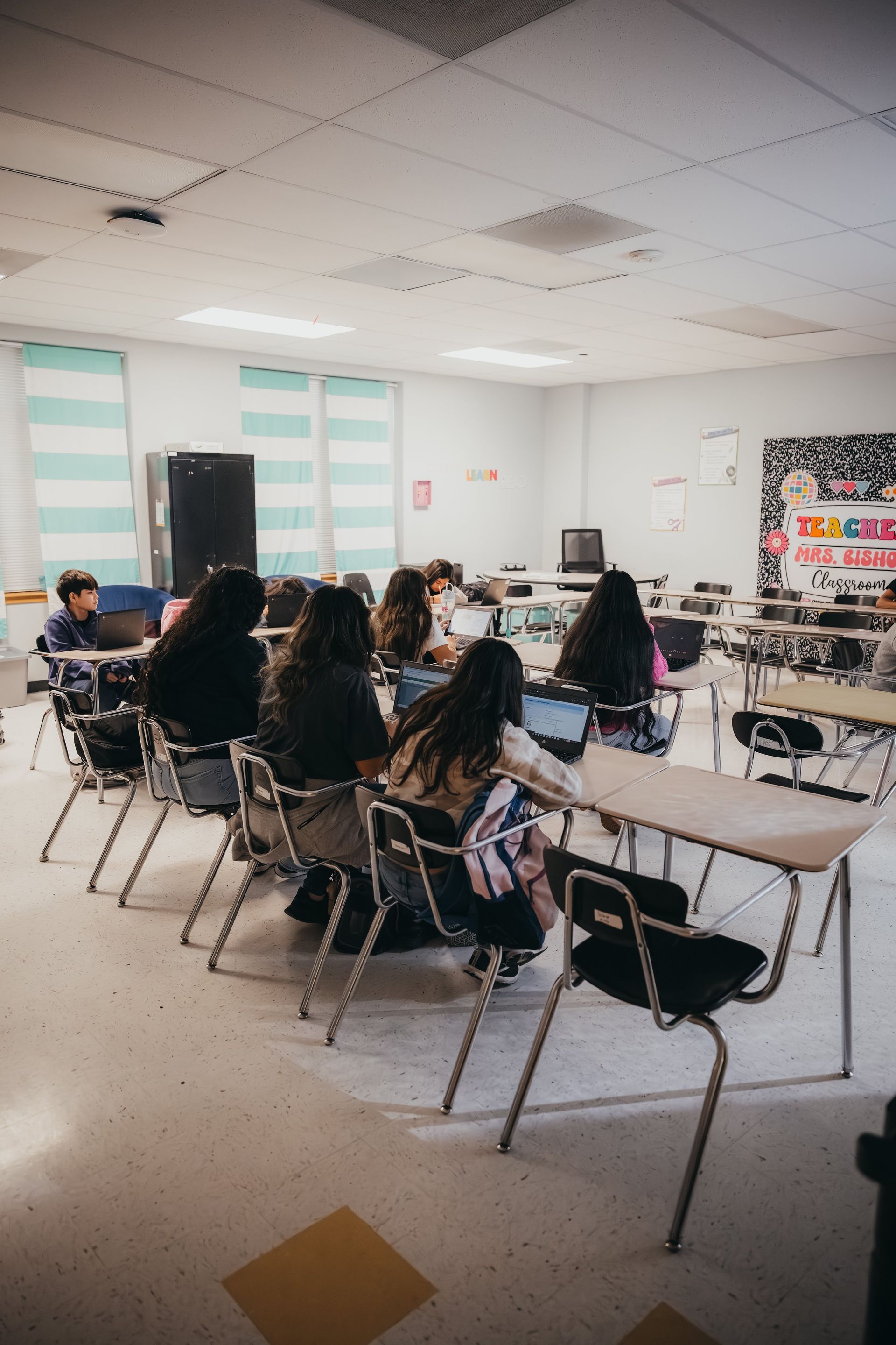 Students working on laptops in a classroom, seated at individual desks.