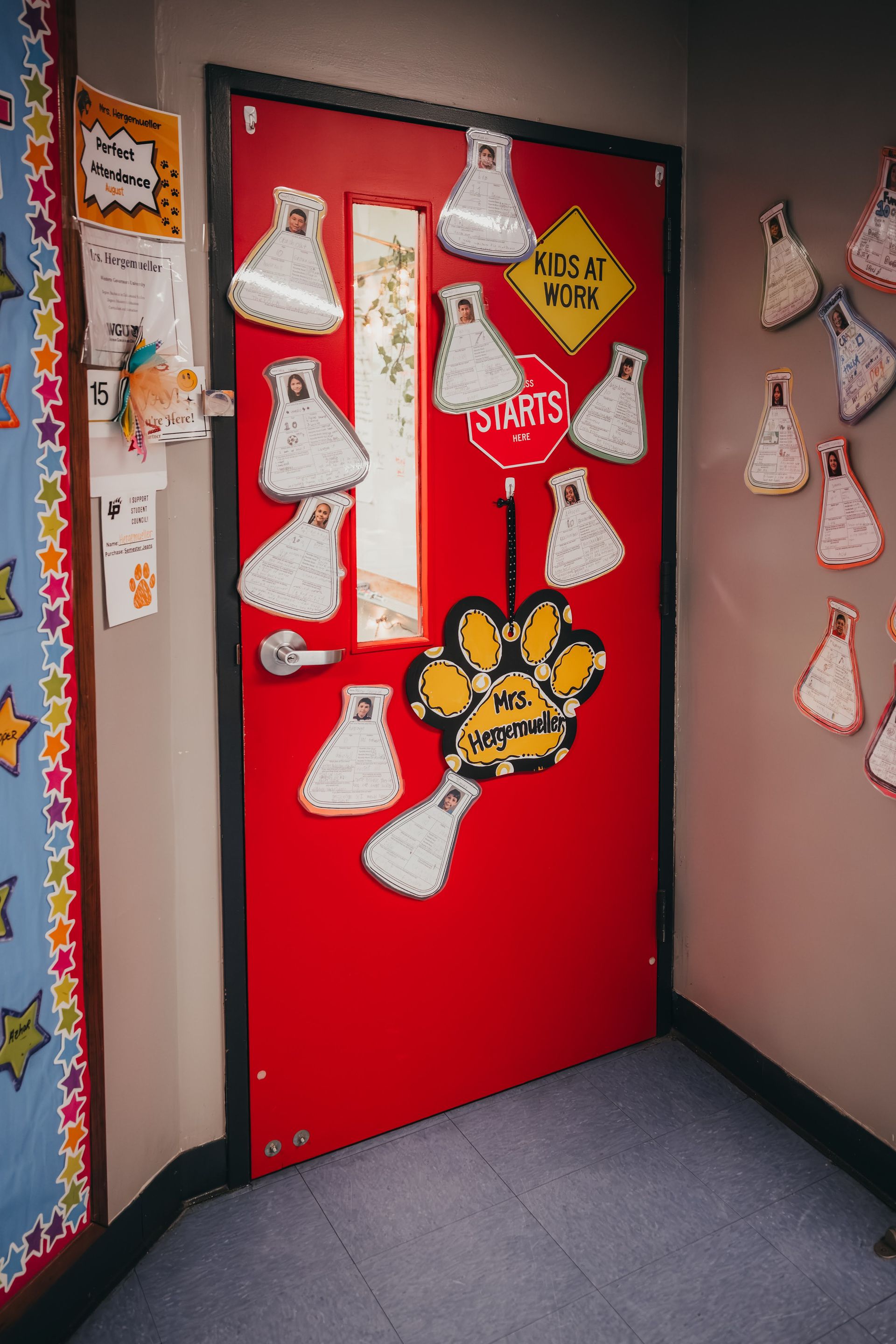 Red classroom door decorated with science flask cutouts and a paw print sign.