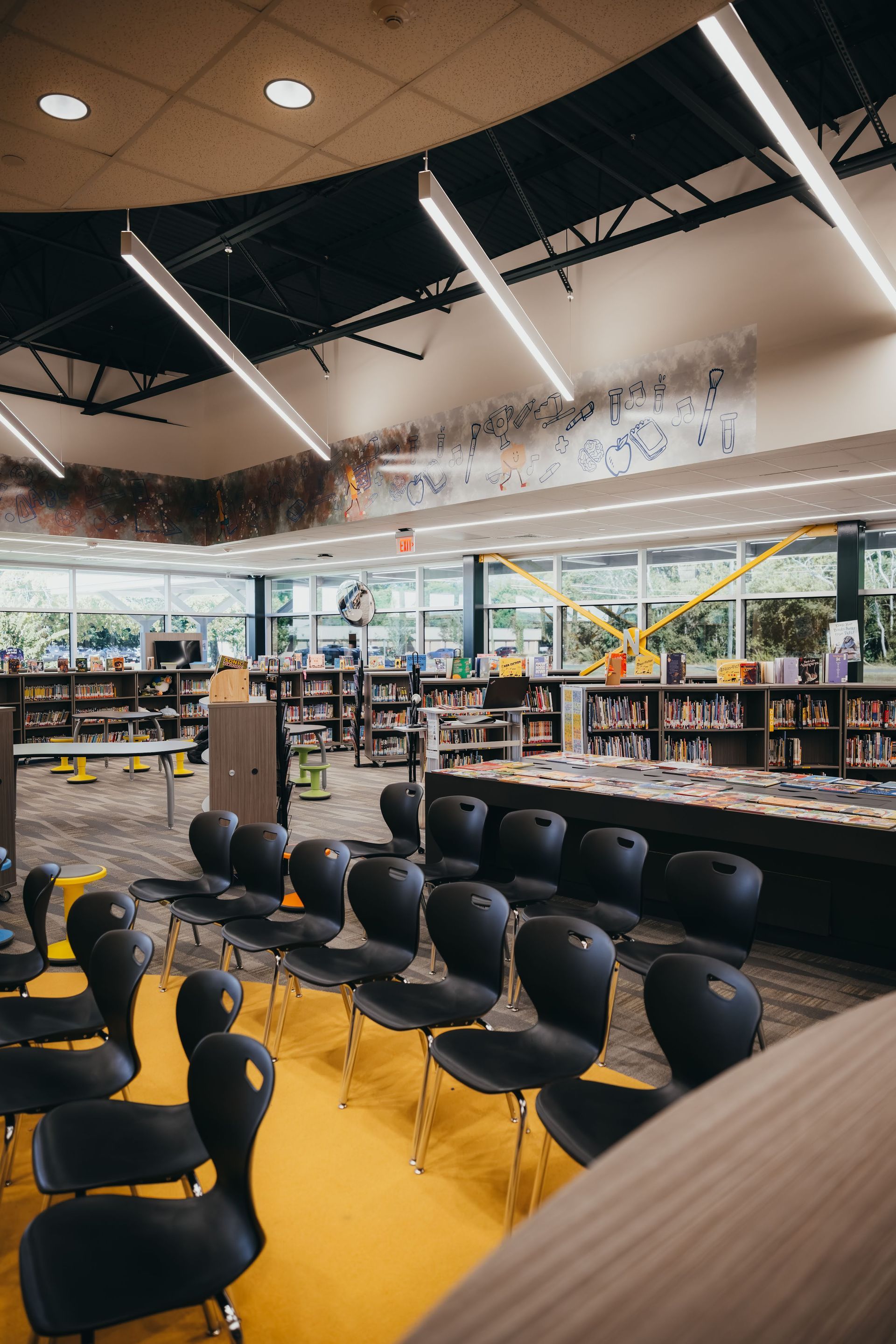 Library interior with rows of black chairs, bookshelves, and a yellow floor.