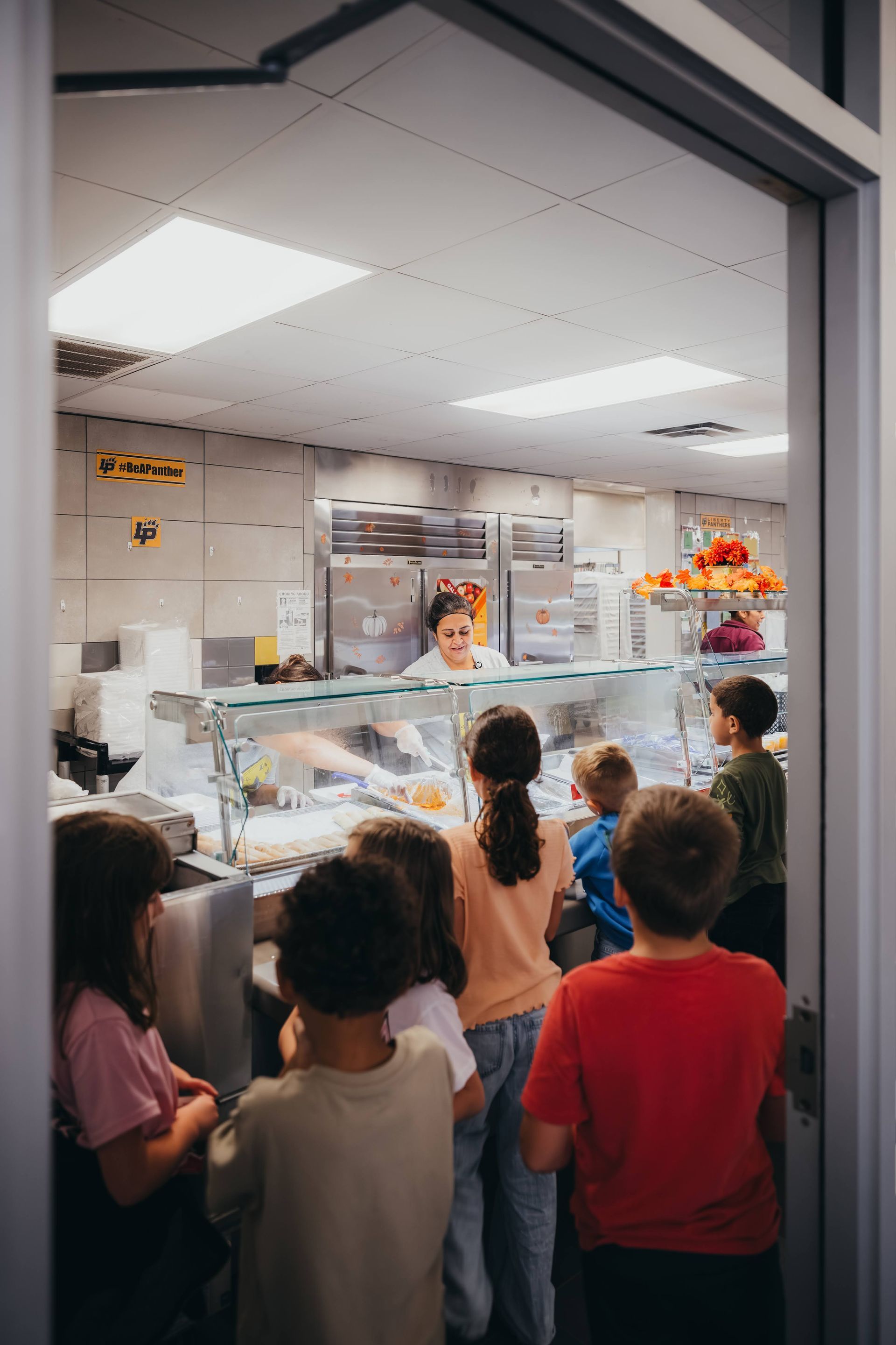 Children lined up at a school cafeteria lunch counter, looking at food choices.