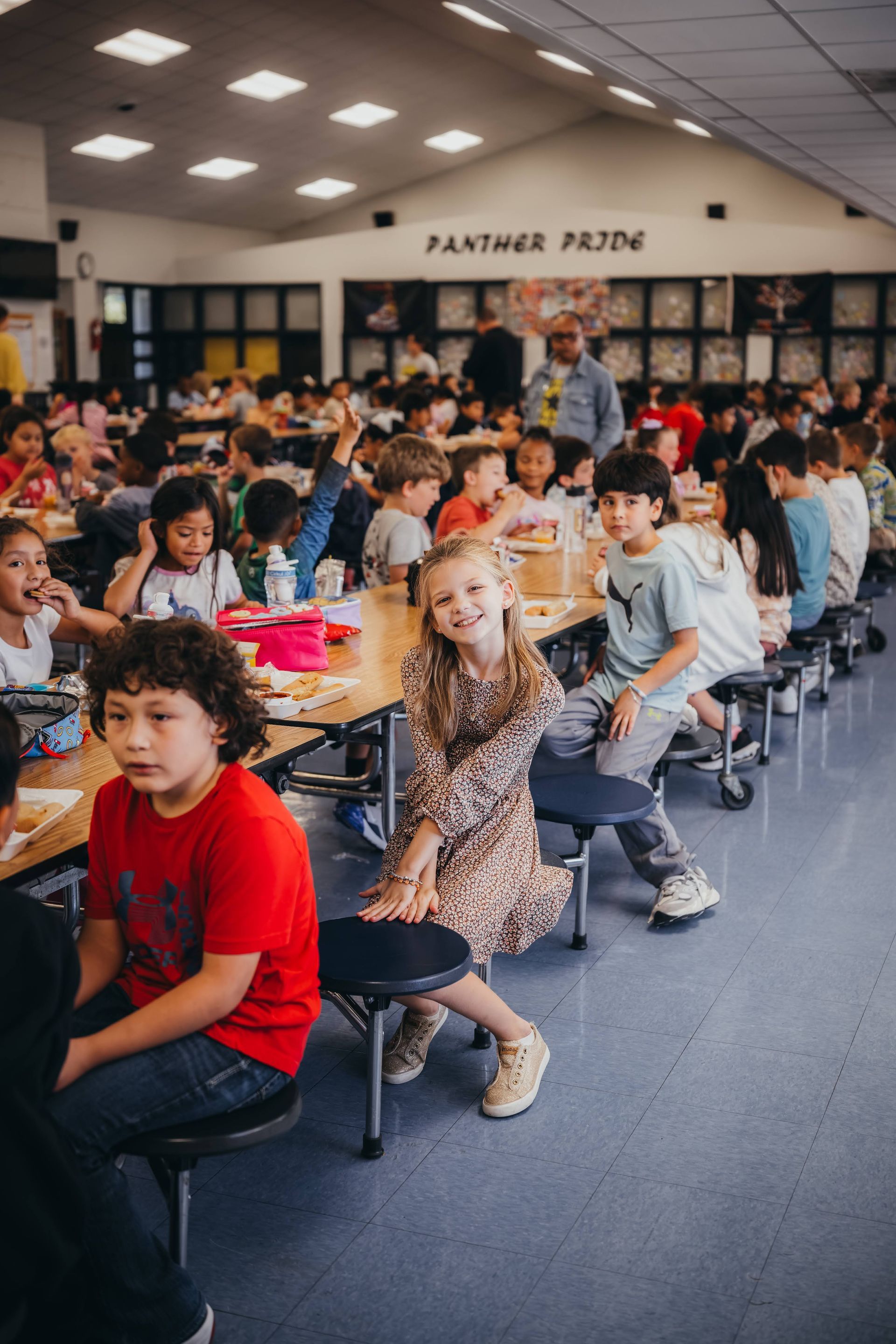 Children eating lunch at tables in a school cafeteria; 