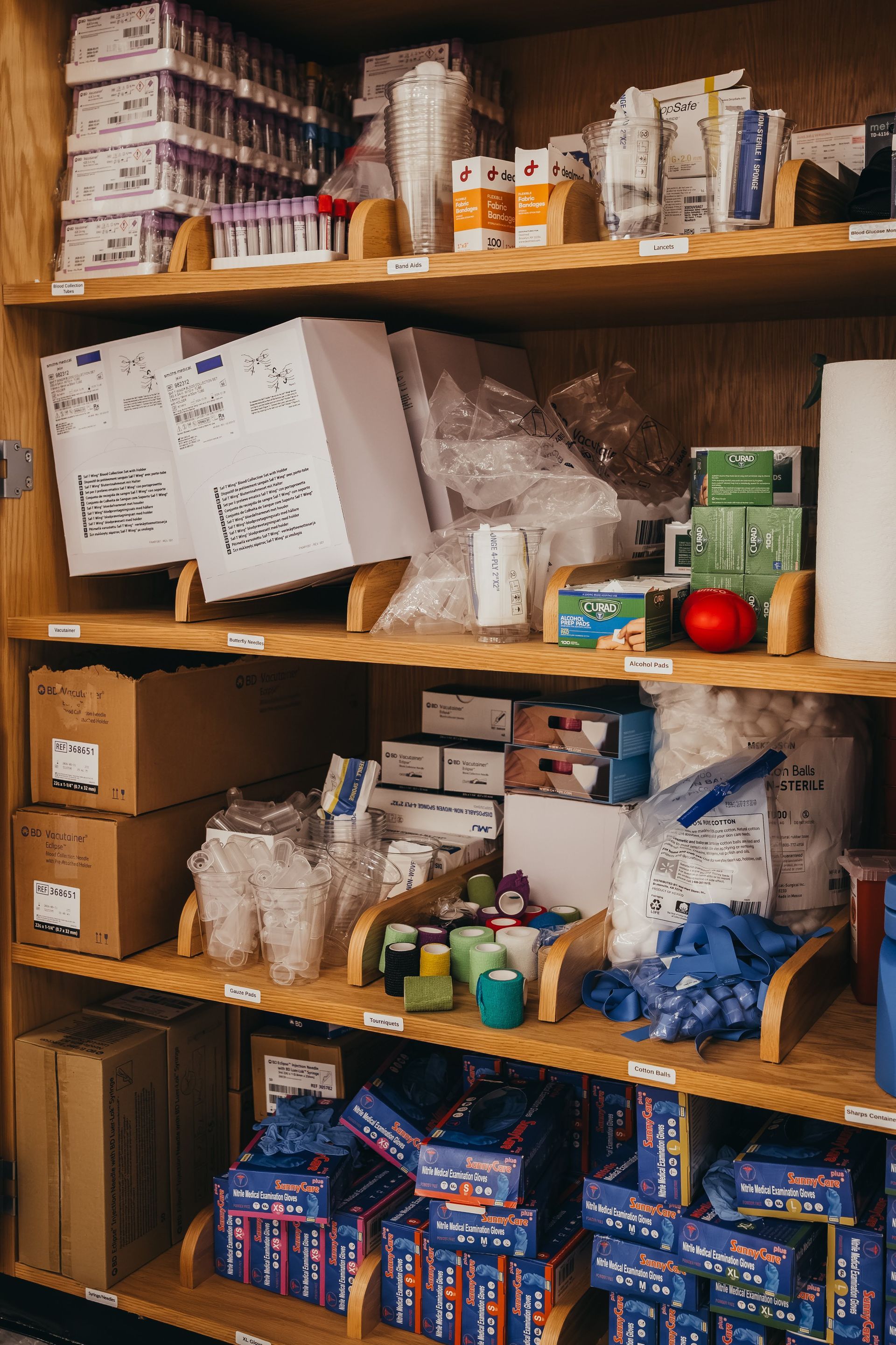 Shelves in a medical supply cabinet filled with various items, including boxes, vials, and cups.