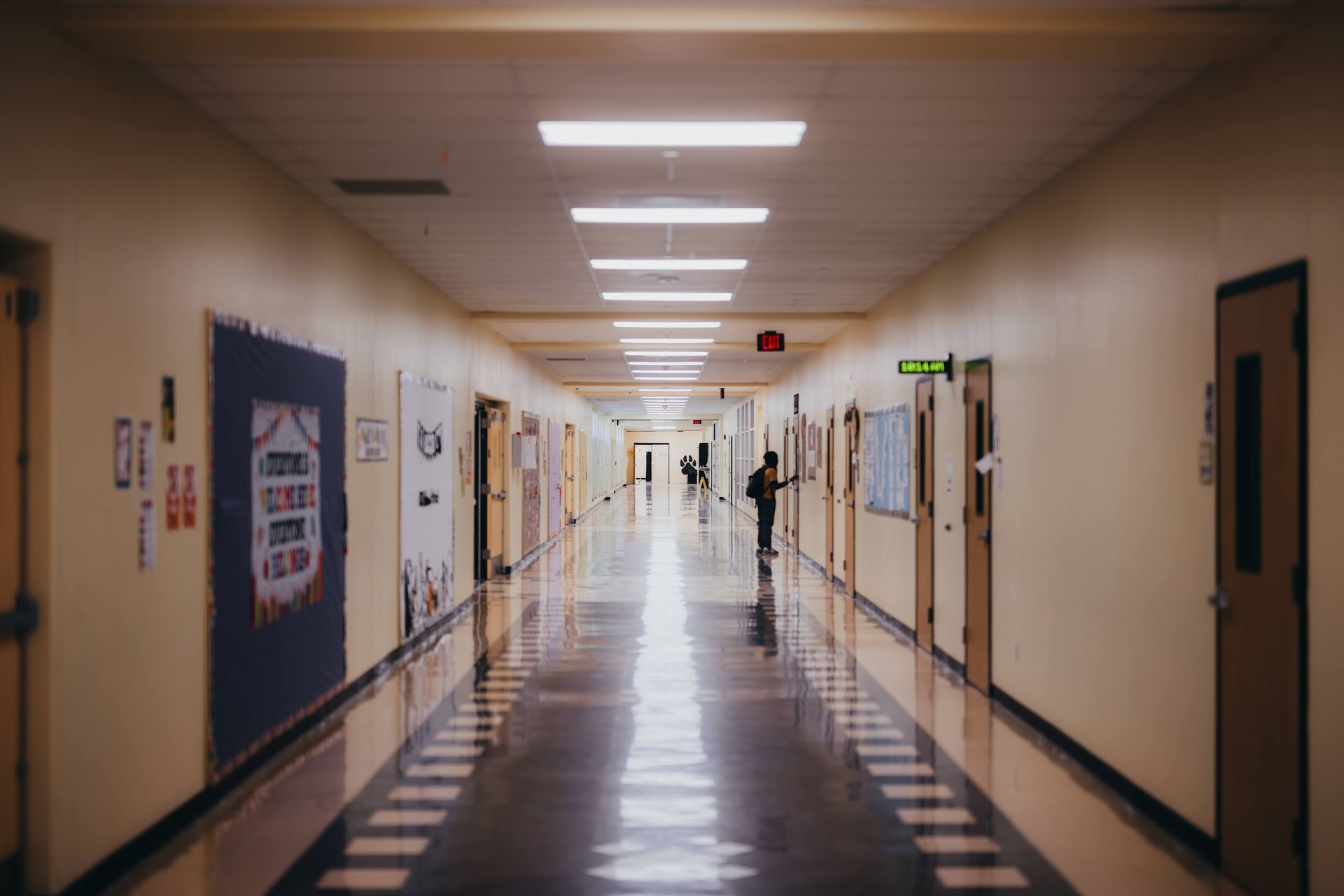 Long school hallway with closed doors and posters, a student in the distance.