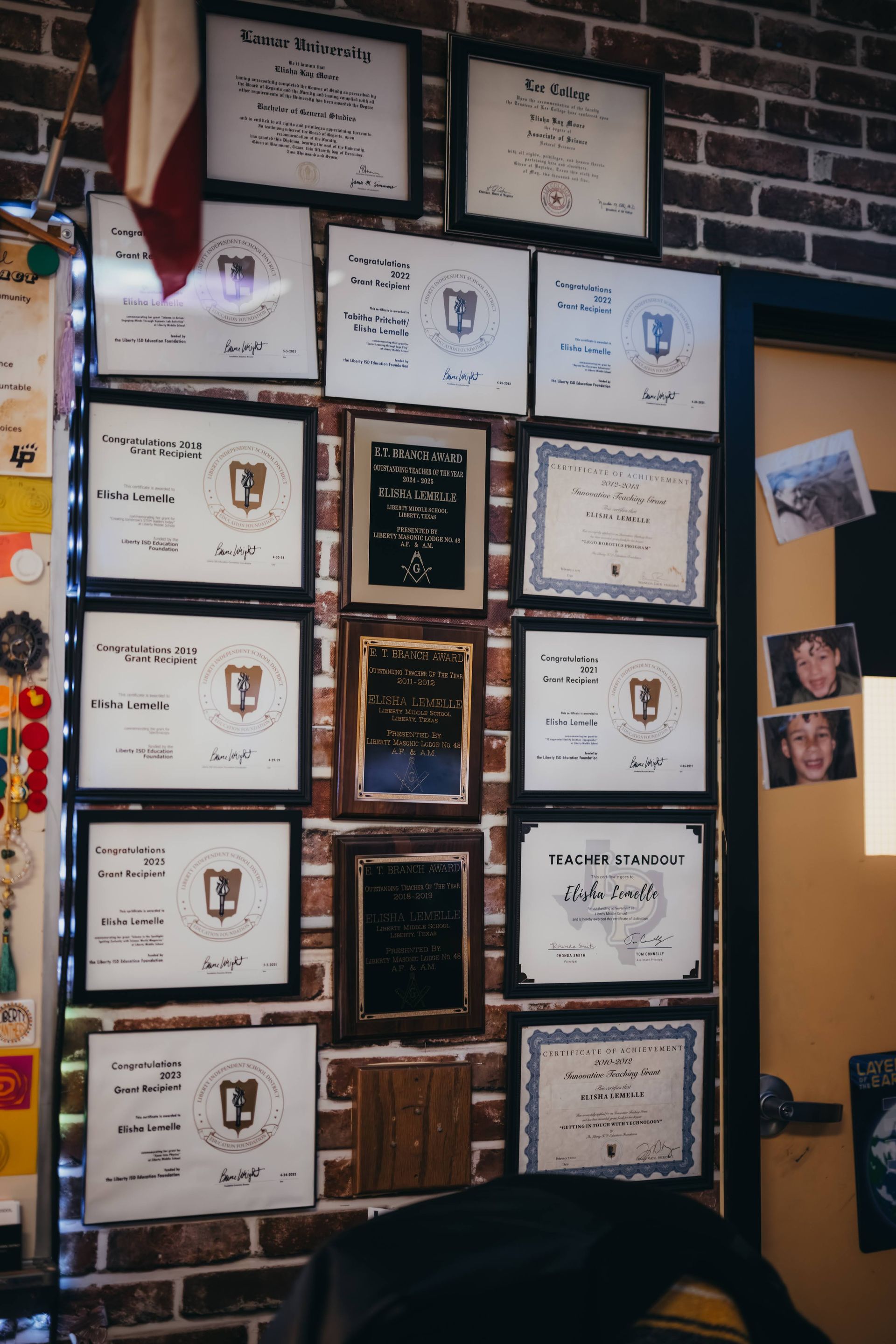Certificates framed on a brick wall, near a door. A flag hangs above the frames.