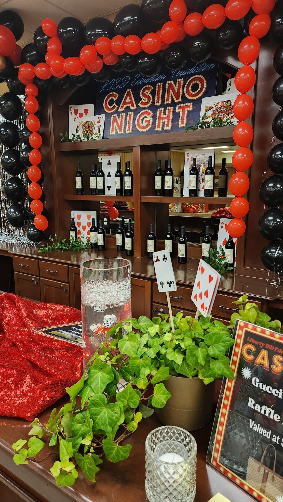 Casino night bar with red and black balloons, playing card decorations, and a sign.