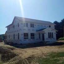 White two-story house under bright sunlight with a porch and dirt yard