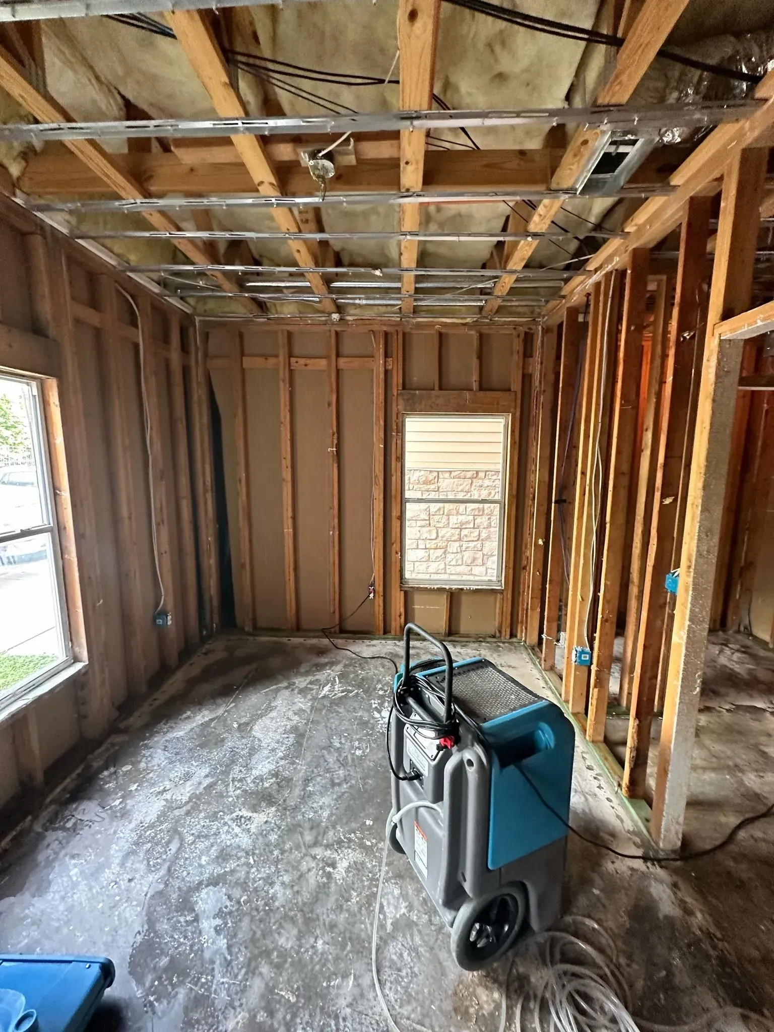 Interior view of a room under construction with exposed wood framing, a dehumidifier, and two windows.
