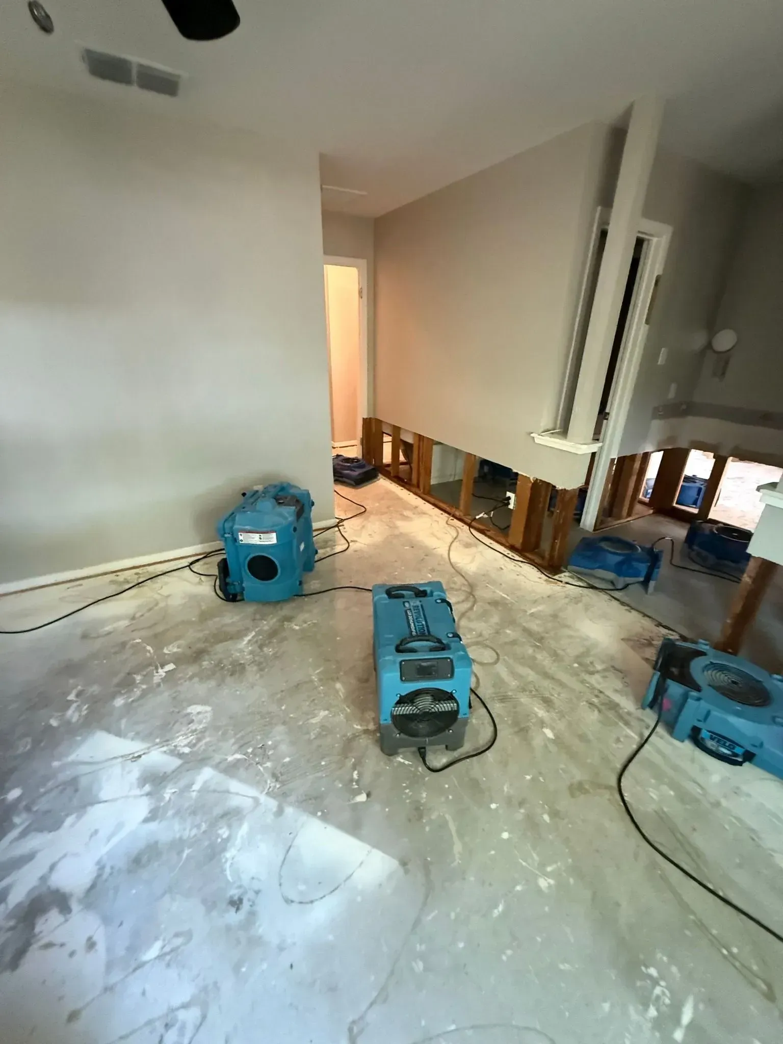 Blue dehumidifiers drying a flooded room, exposed wall studs, debris on floor.