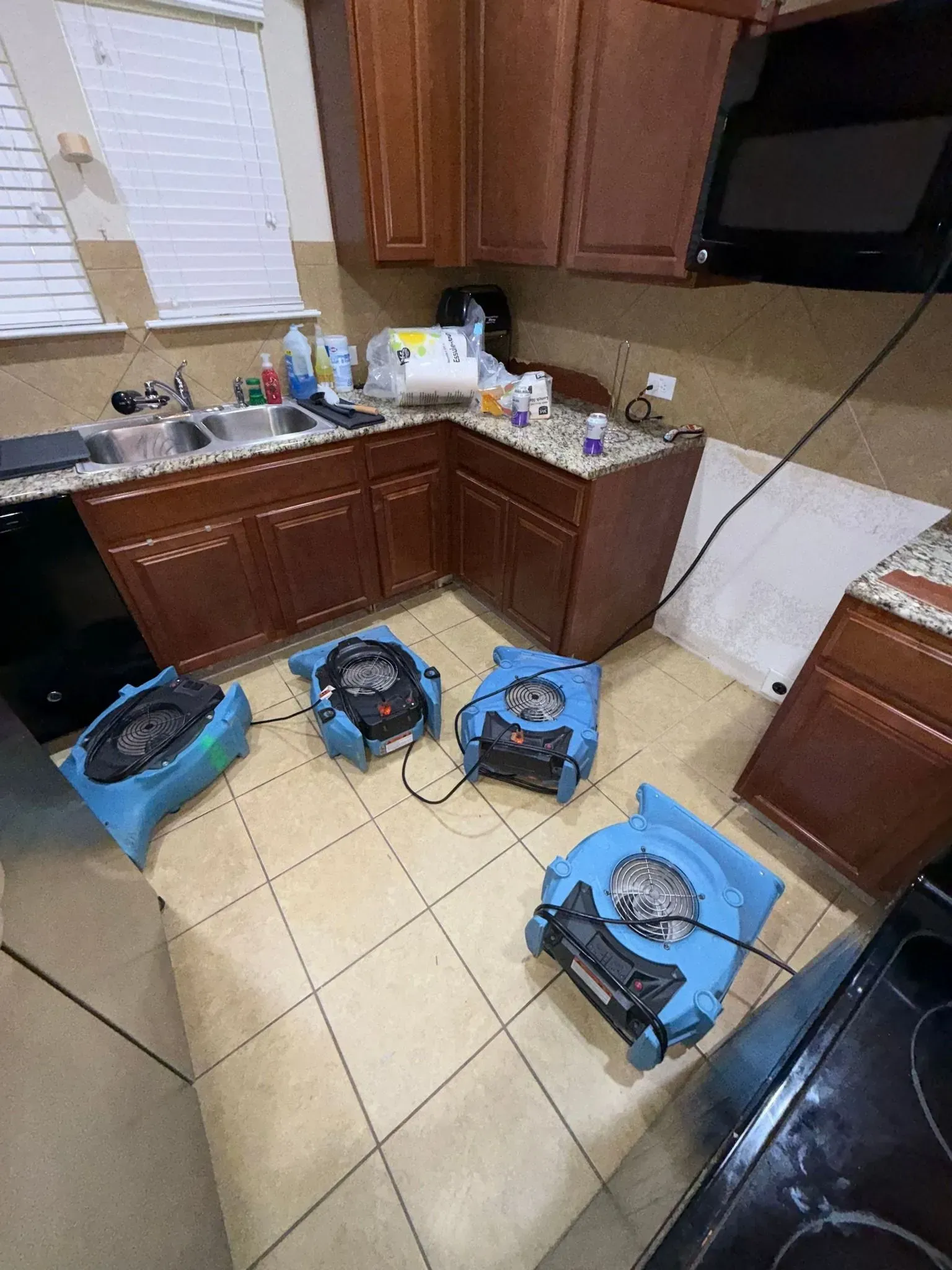 Kitchen with four blue air movers on tile floor, cabinets, sink, and an oven.