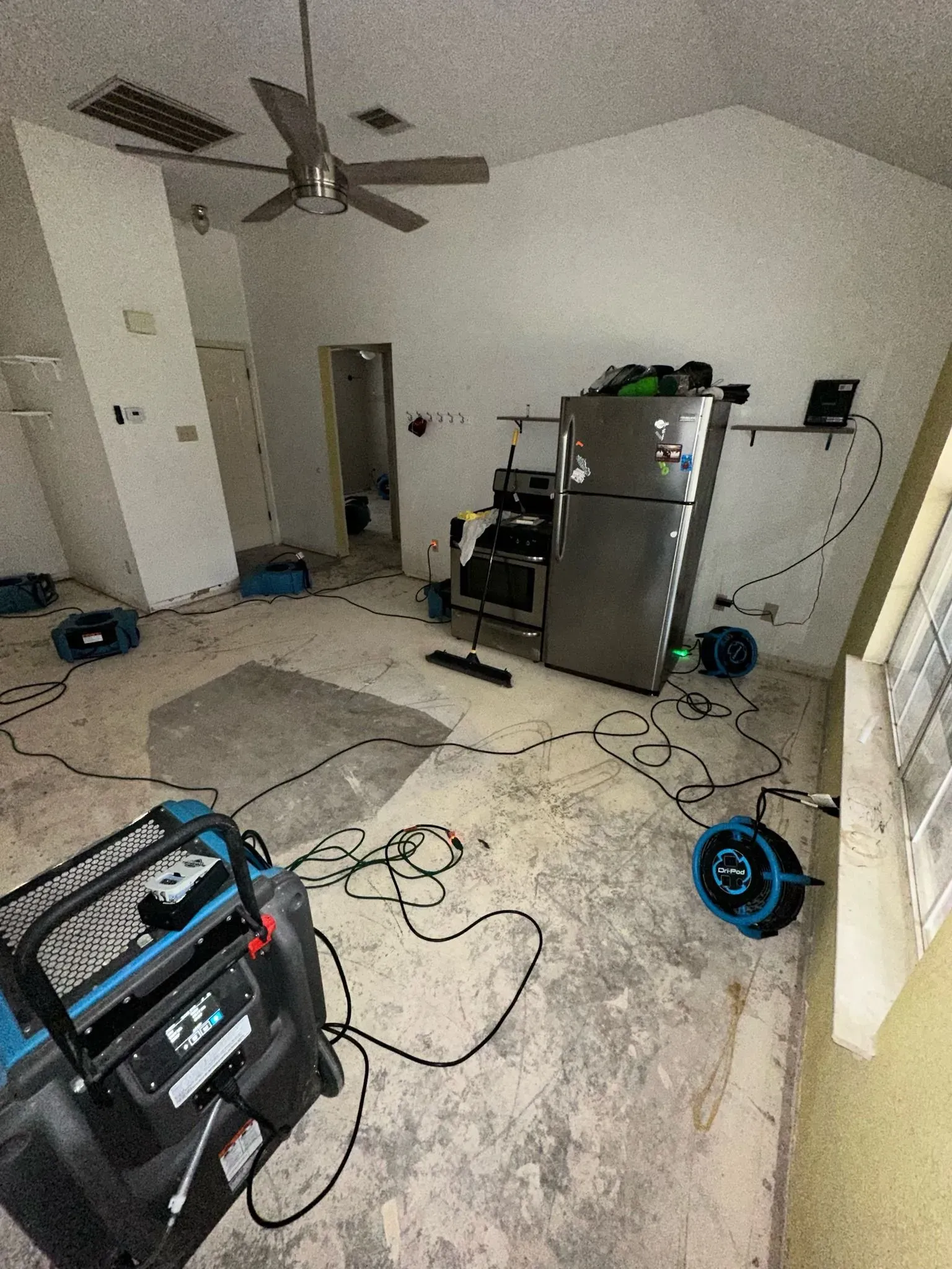 A room being dried out after water damage with equipment including a refrigerator and ceiling fan.