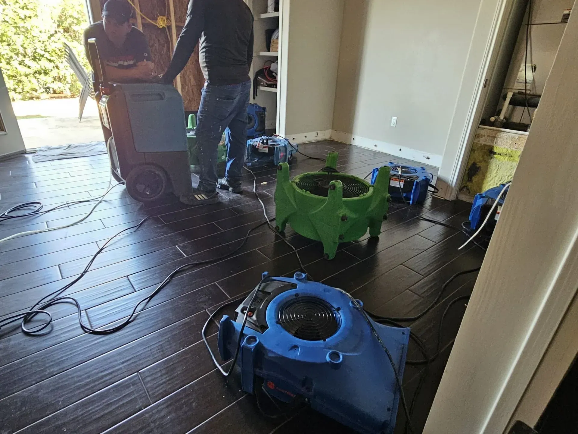 Men with drying equipment in a room, setting up fans to dry a hardwood floor after water damage.