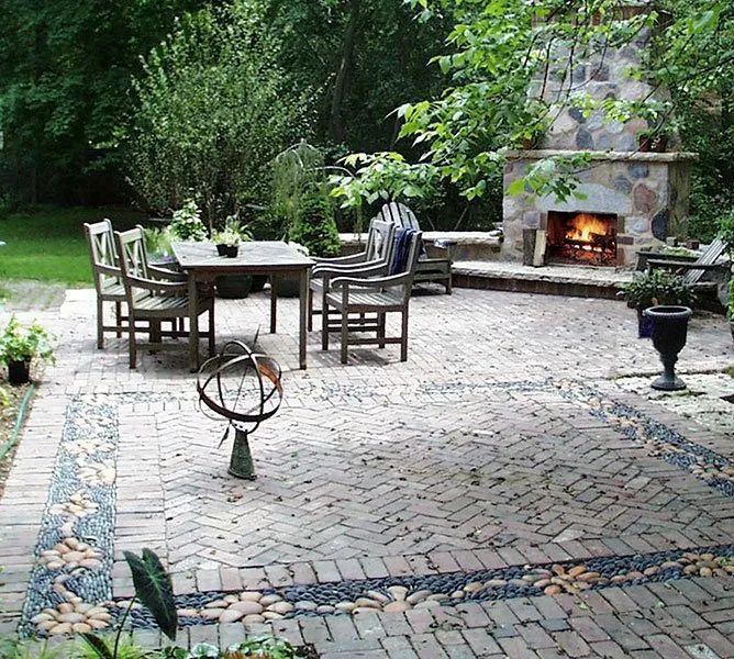 A brick patio with a dining set and fireplace, featuring a decorative border of smooth river stones set in the ground.