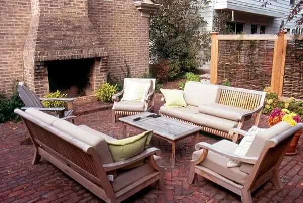 Outdoor brick patio with a fireplace, comfortable wooden lounge seating, and a coffee table.