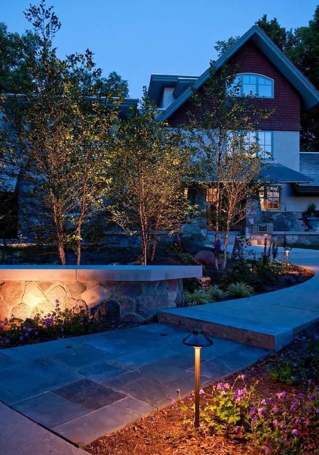 A house exterior at dusk, featuring a stone path, illuminated landscaping, and warm garden lighting.