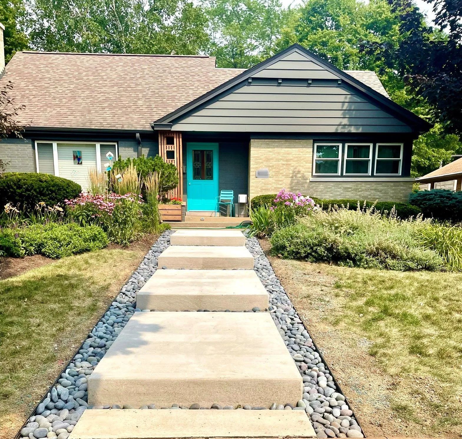 A house with stone and dark gray siding, a bright turquoise front door, and a modern floating concrete walkway.