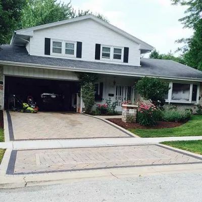 A two-story white house with a dark roof and a patterned stone driveway leading to an open two-car garage.