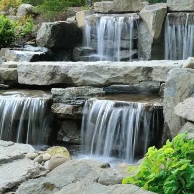 A tiered stone waterfall flowing into a pool surrounded by greenery.