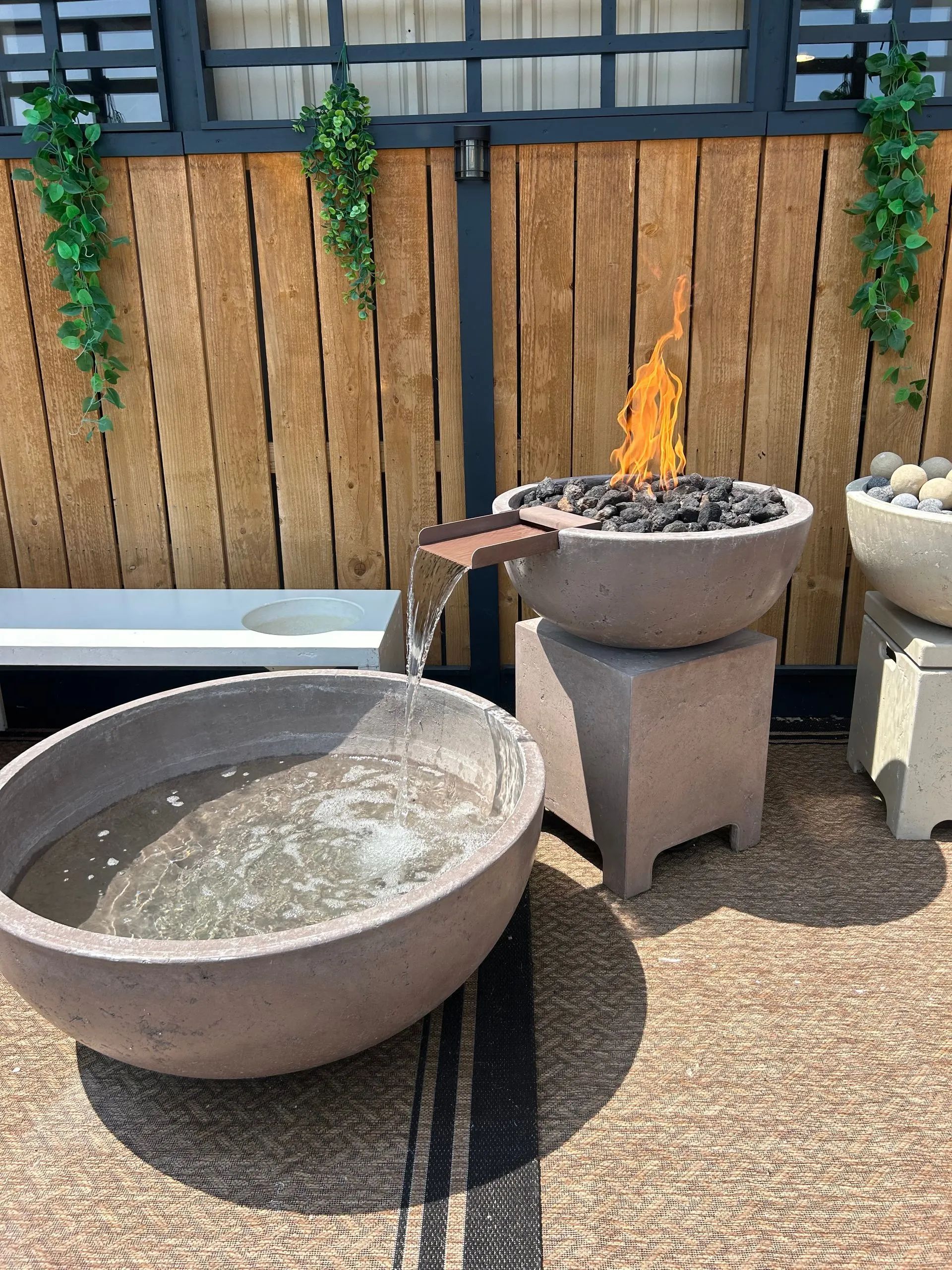 A fire and water feature with a burning flame pouring water from a concrete bowl into a larger basin on a patio.