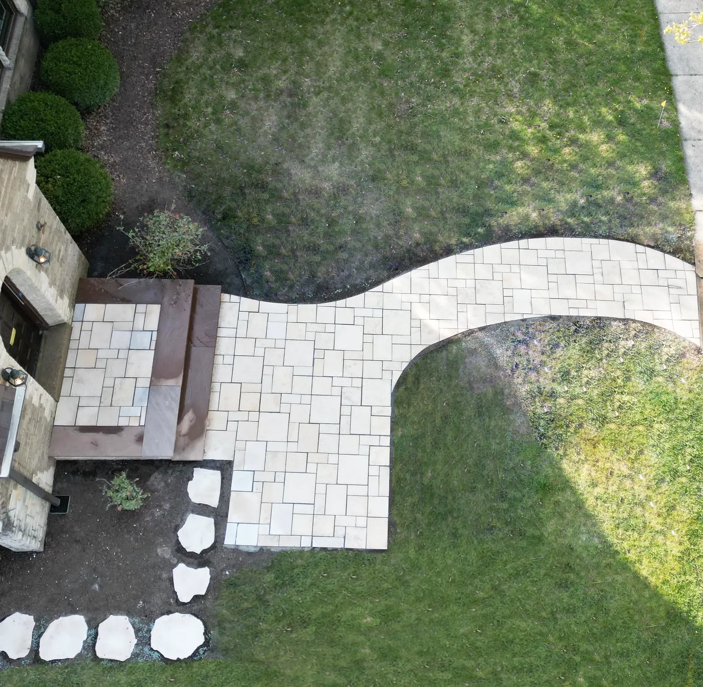 An aerial view of a stone pathway leading from a house entrance across a grassy lawn with a small stone-bordered garden.