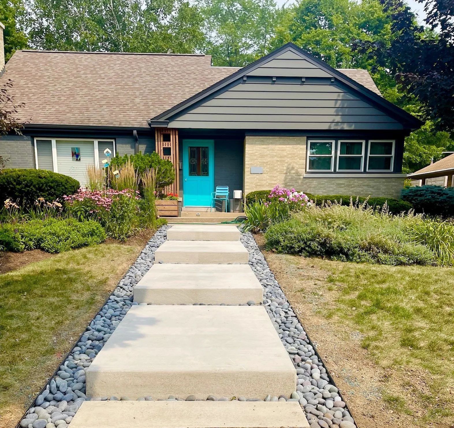 A light-colored house with a dark roof and vibrant blue front door, reached by a concrete walkway lined with gray stones.