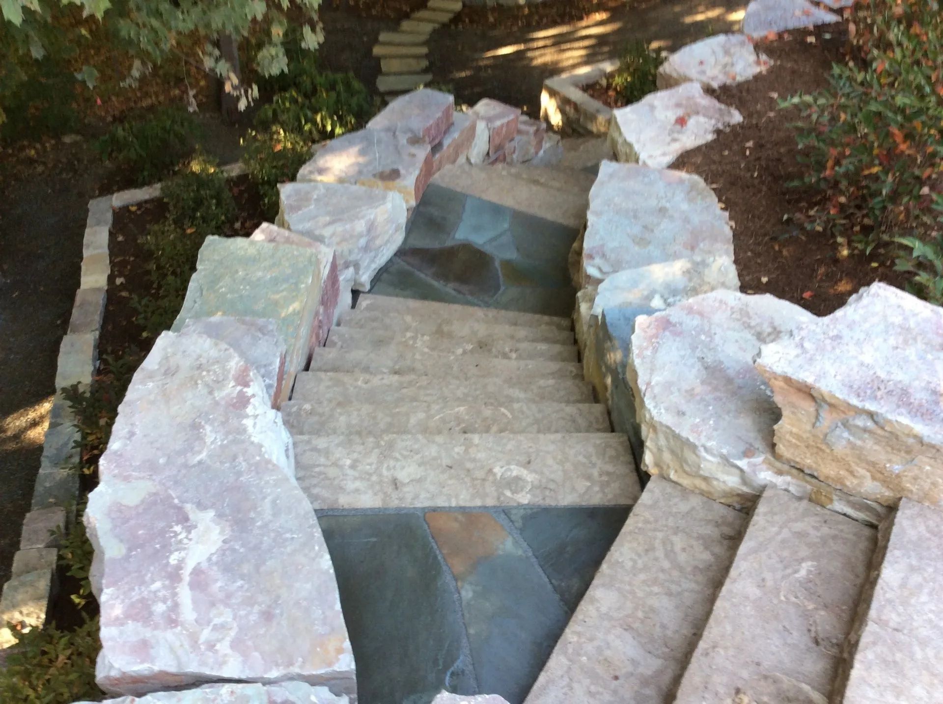 Outdoor stone staircase built with large, light-colored rock borders descending into a garden pathway.