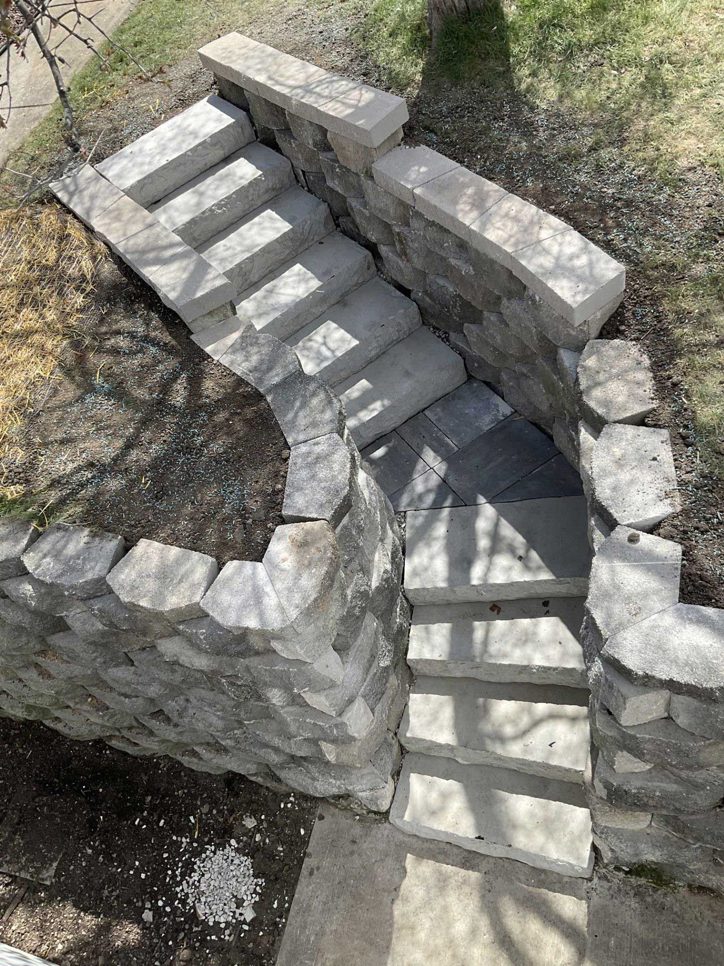 A high-angle view of stone stairs curving down through a landscaped yard, framed by stacked stone retaining walls.