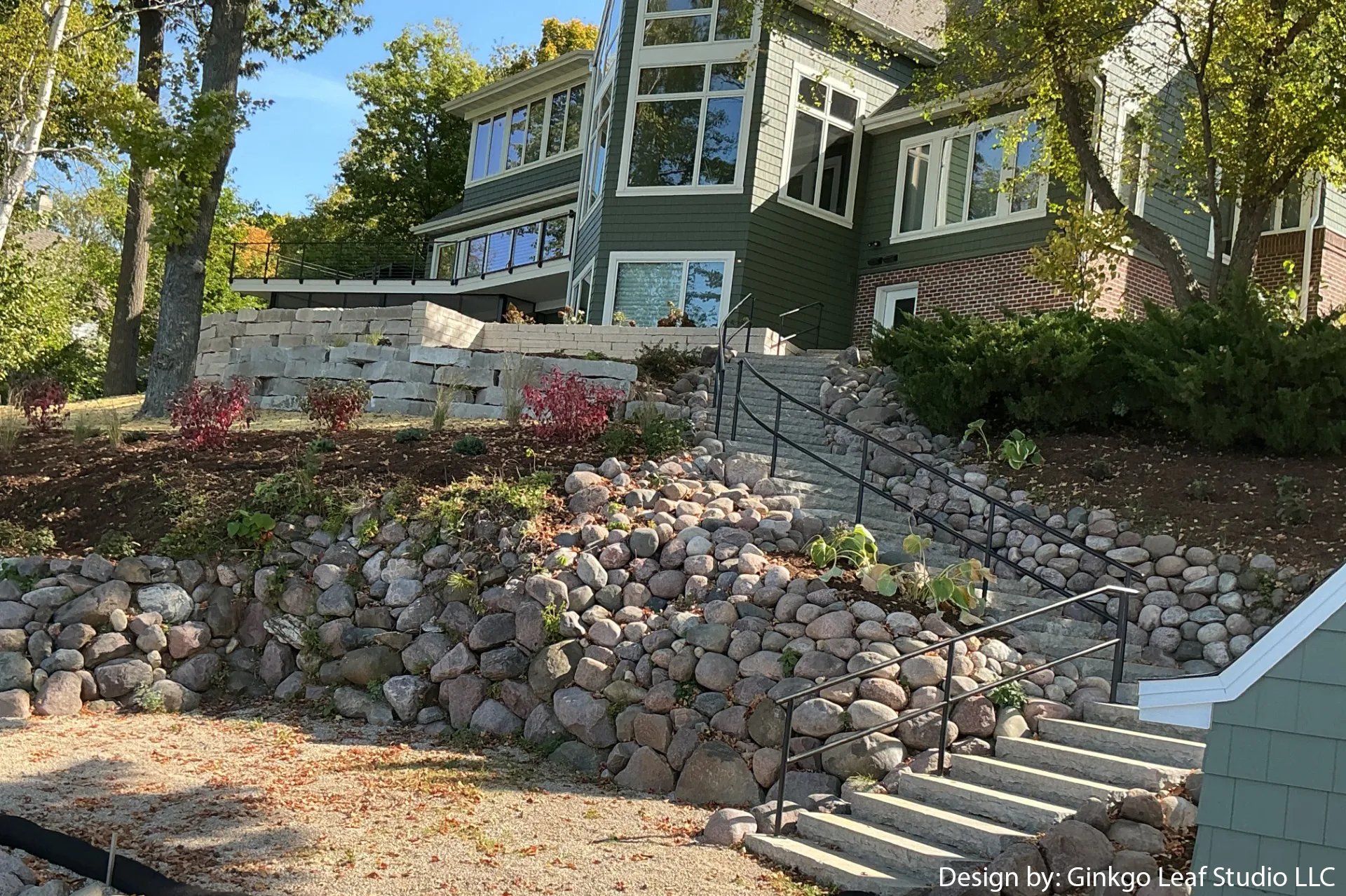 A multi-level home with a large stone retaining wall and a set of stone steps leading up the sloped landscape.