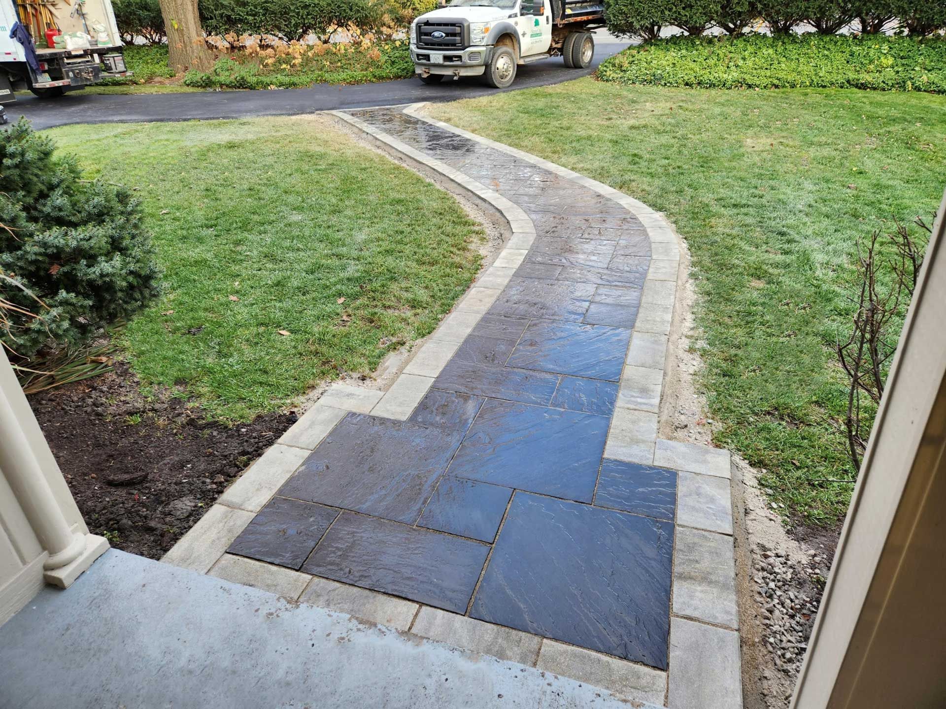 A newly installed dark stone walkway with a light-colored stone border leading through a green grassy lawn.