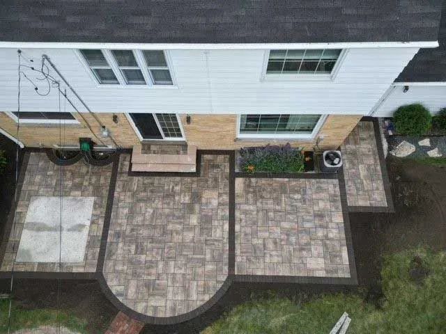 An aerial view of a multi-section paver patio with a curved edge attached to the back of a two-story house.